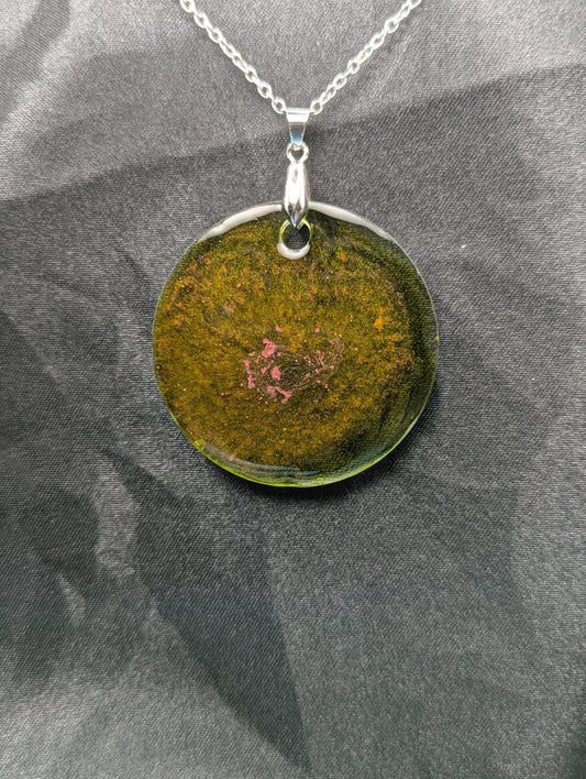 Green circle resin pendant with coral pink specks & swirls & an internal color that looks yellow/orange. Resin pendant on a silver pinch bail & stainless steel chain.