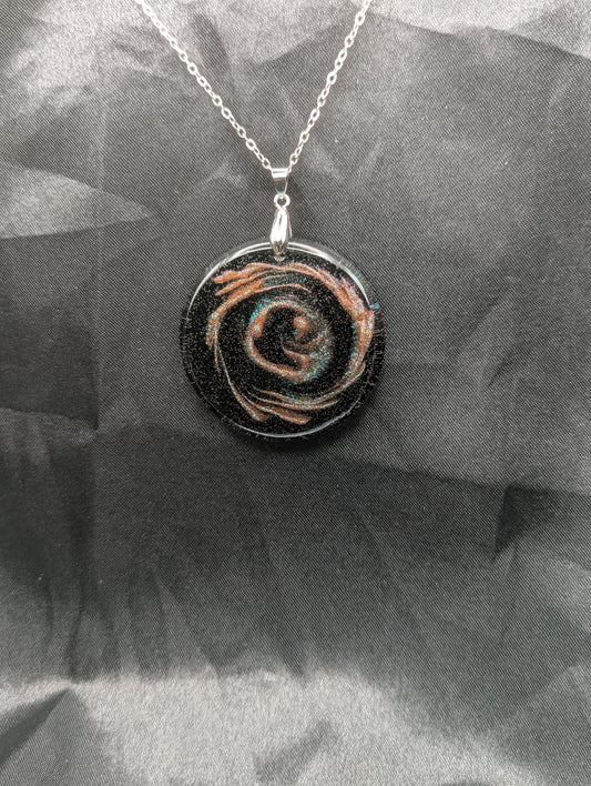 Black Resin Circle Pendant with coral-pink colored sparkly swirls inside on a silver pinch bail & stainless steel chain.