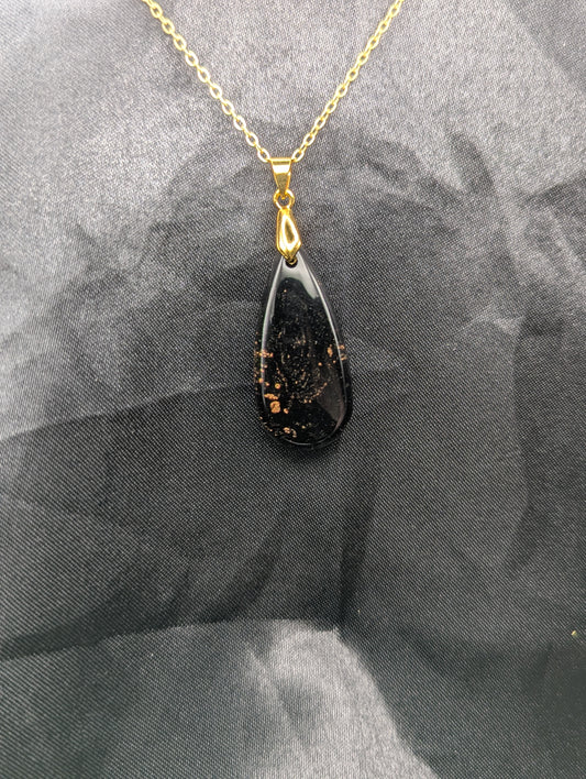 Black Resin Teardrop Pendant with specks of sparkly gold swirled inside. Pendant is on a gold pinch bail & gold plated metal chain.