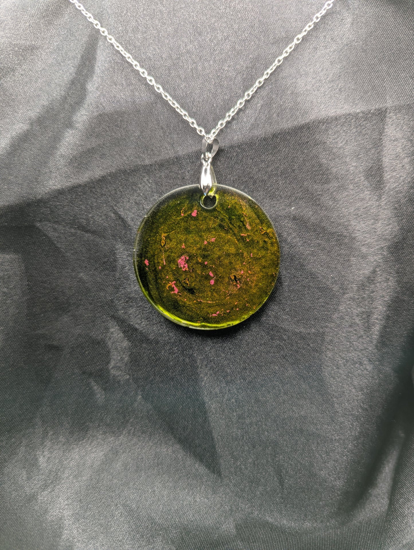 Back view of Green circle resin pendant with coral pink specks & swirls & an internal color that looks yellow/orange. Resin pendant on a silver pinch bail & stainless steel chain.
