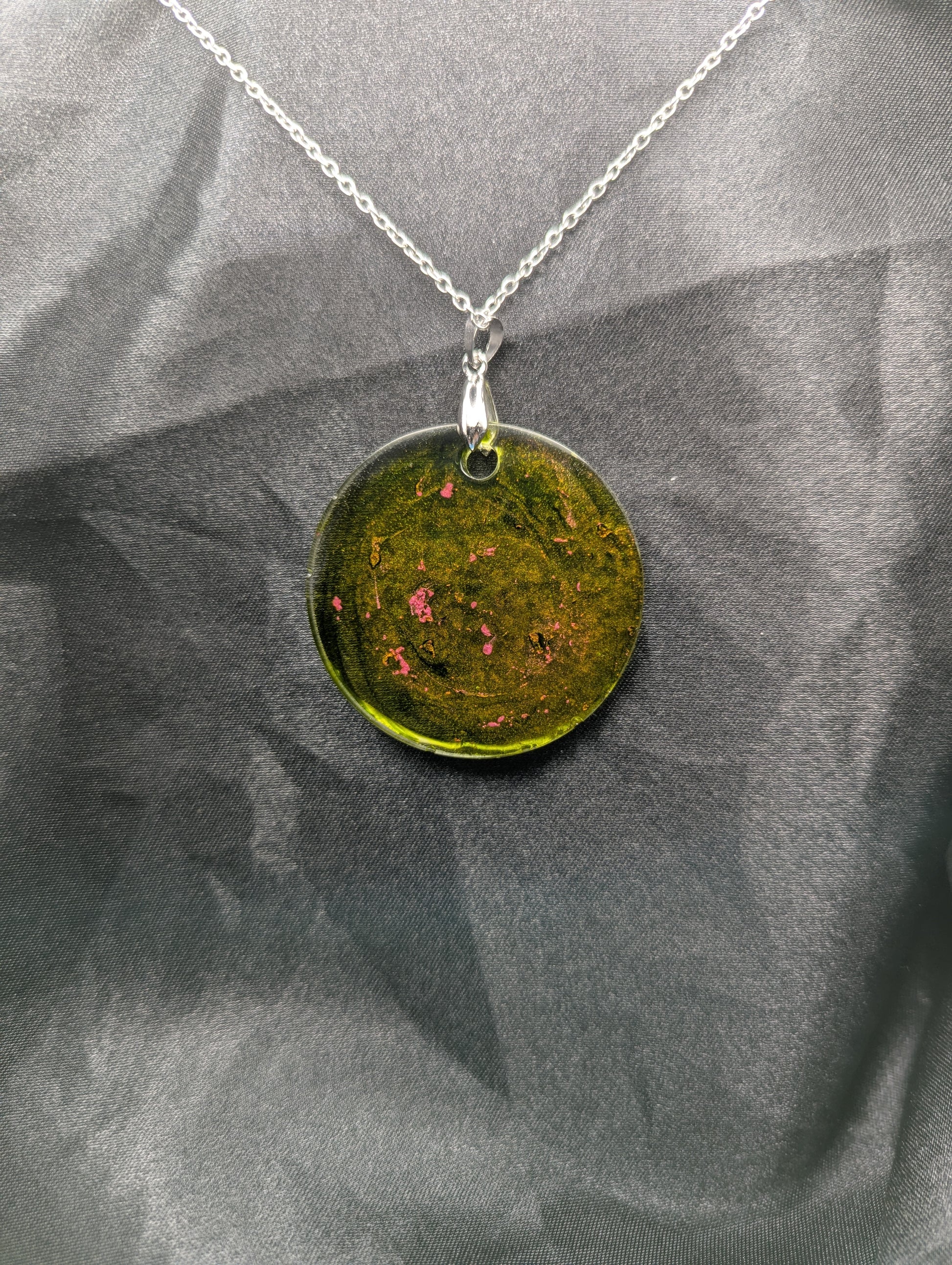 Back view of Green circle resin pendant with coral pink specks & swirls & an internal color that looks yellow/orange. Resin pendant on a silver pinch bail & stainless steel chain.
