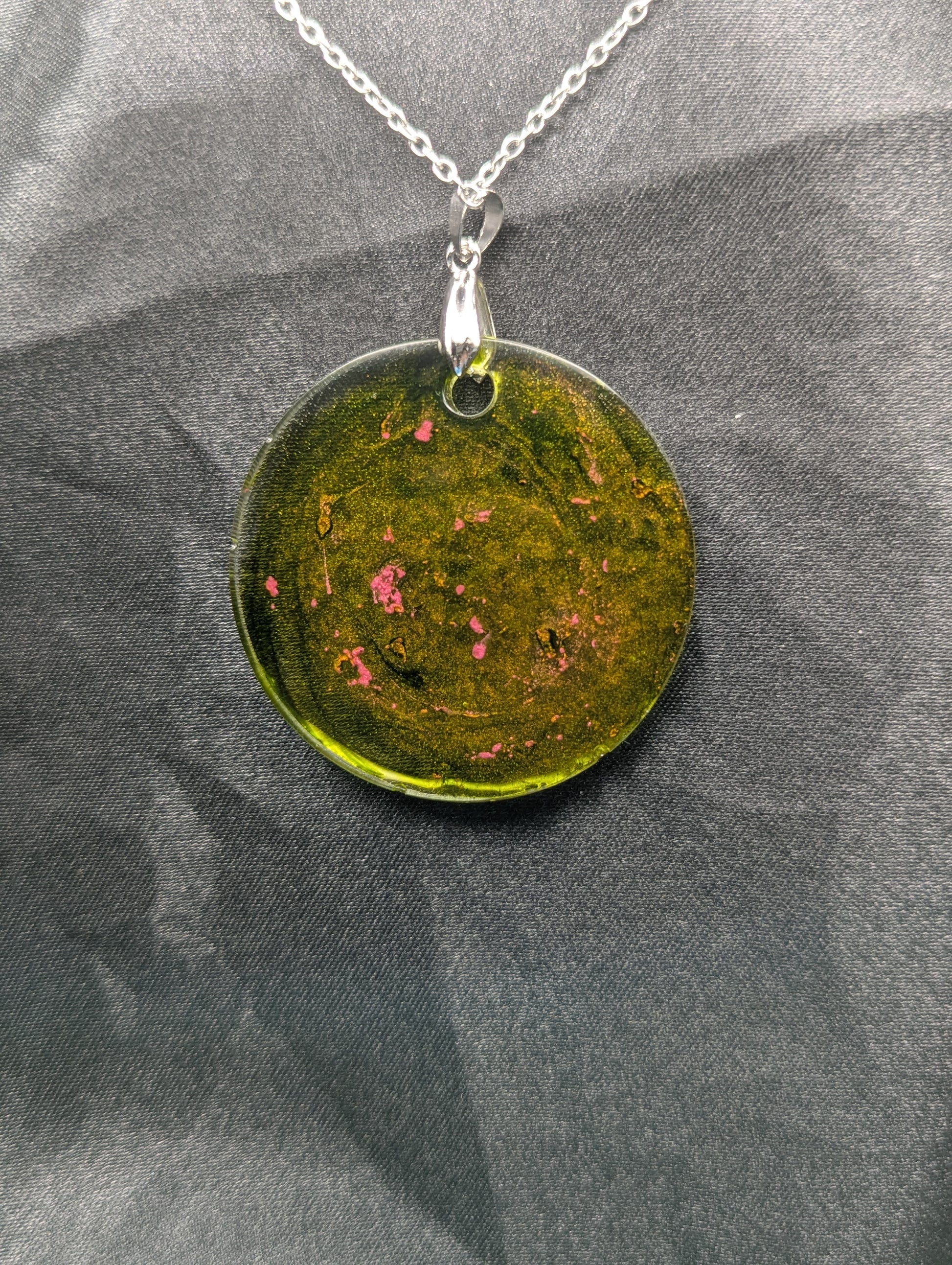 Back view of Green circle resin pendant with coral pink specks & swirls & an internal color that looks yellow/orange. Resin pendant on a silver pinch bail & stainless steel chain.