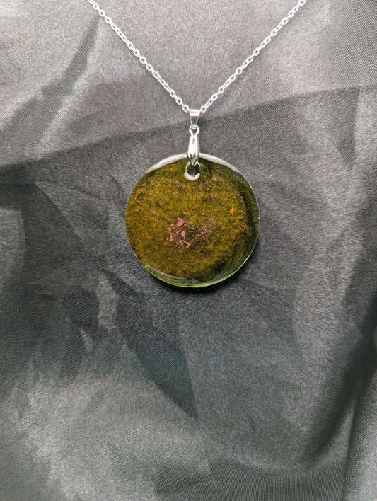 Green circle resin pendant with coral pink specks & swirls & an internal color that looks yellow/orange. Resin pendant on a silver pinch bail & stainless steel chain.