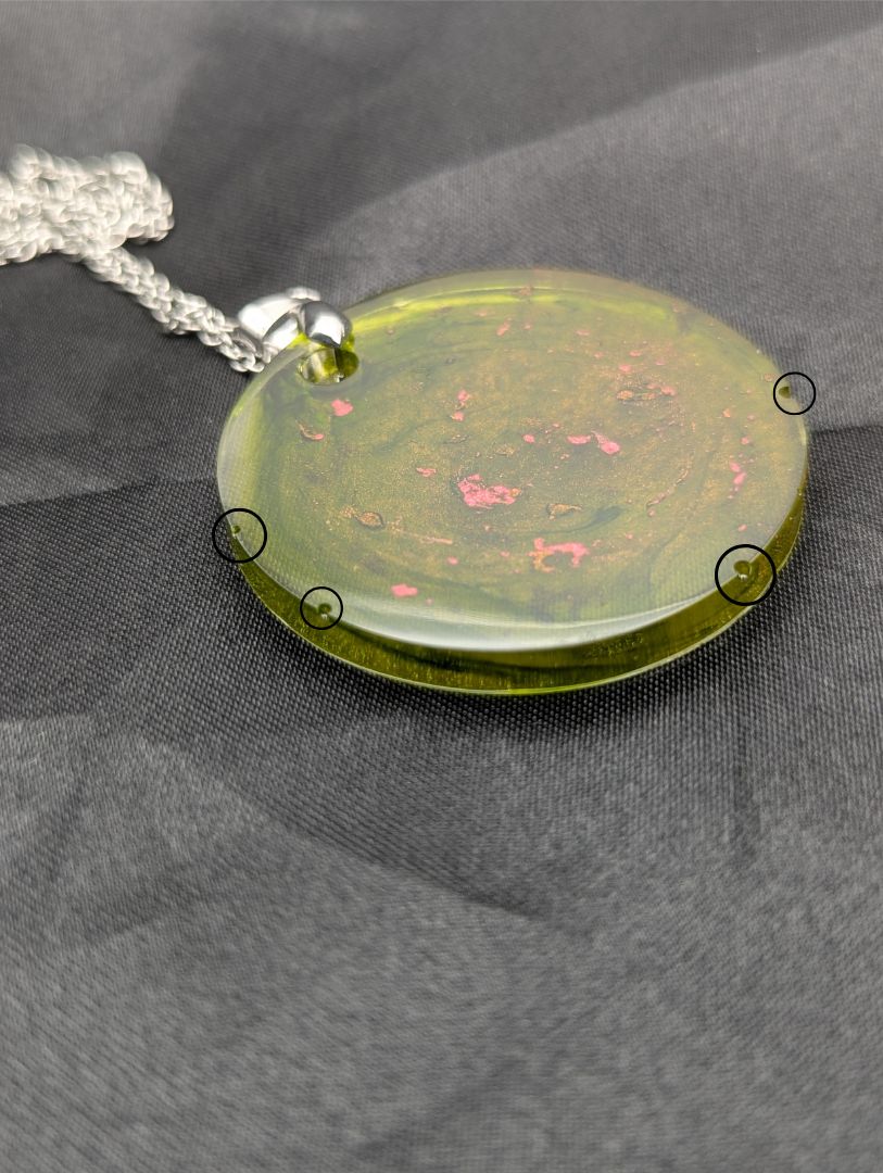 Green circle resin pendant with coral pink specks & swirls & an internal color that looks yellow/orange. Resin pendant on a silver pinch bail & stainless steel chain.