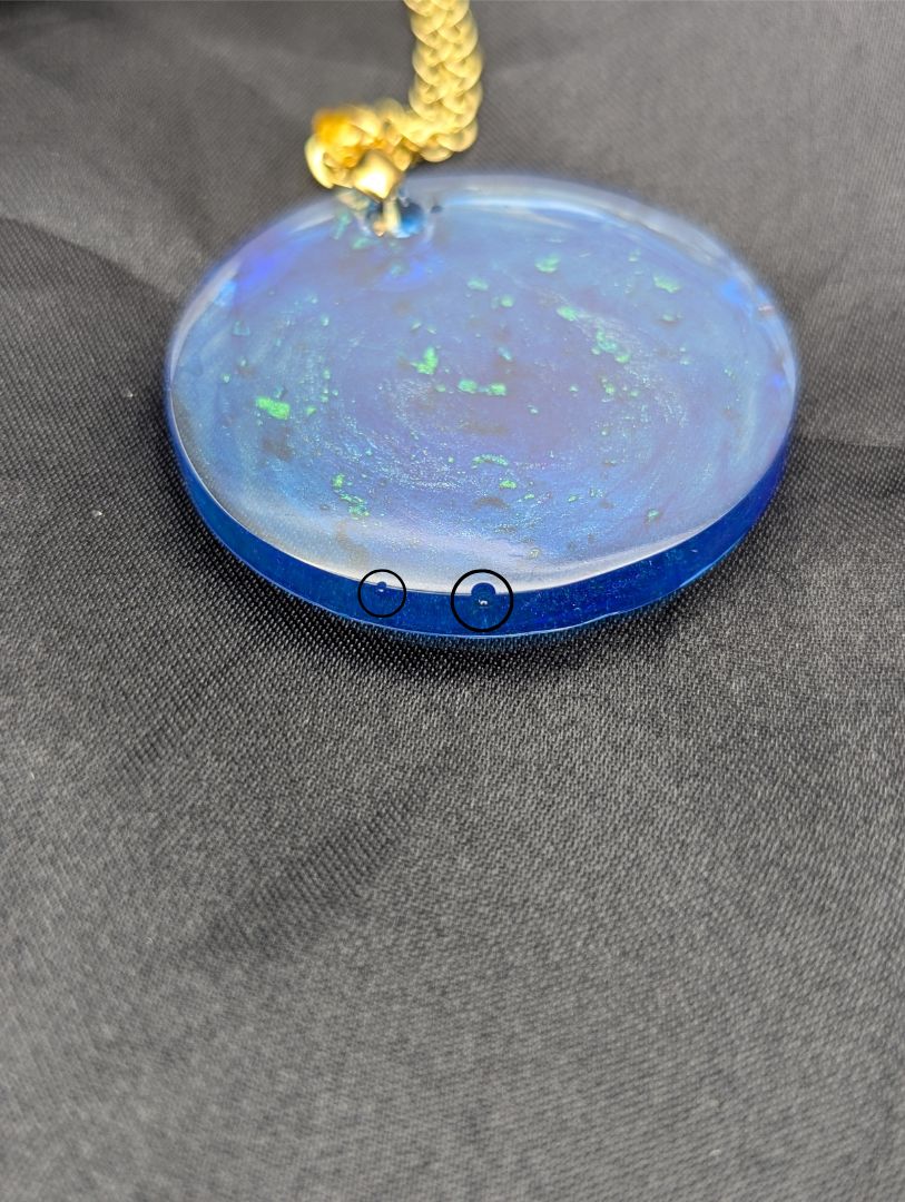 Blue resin circle pendant with speckles & swirls of green pigment powder. Resin necklace on a gold pinch bail and gold plated metal chain.