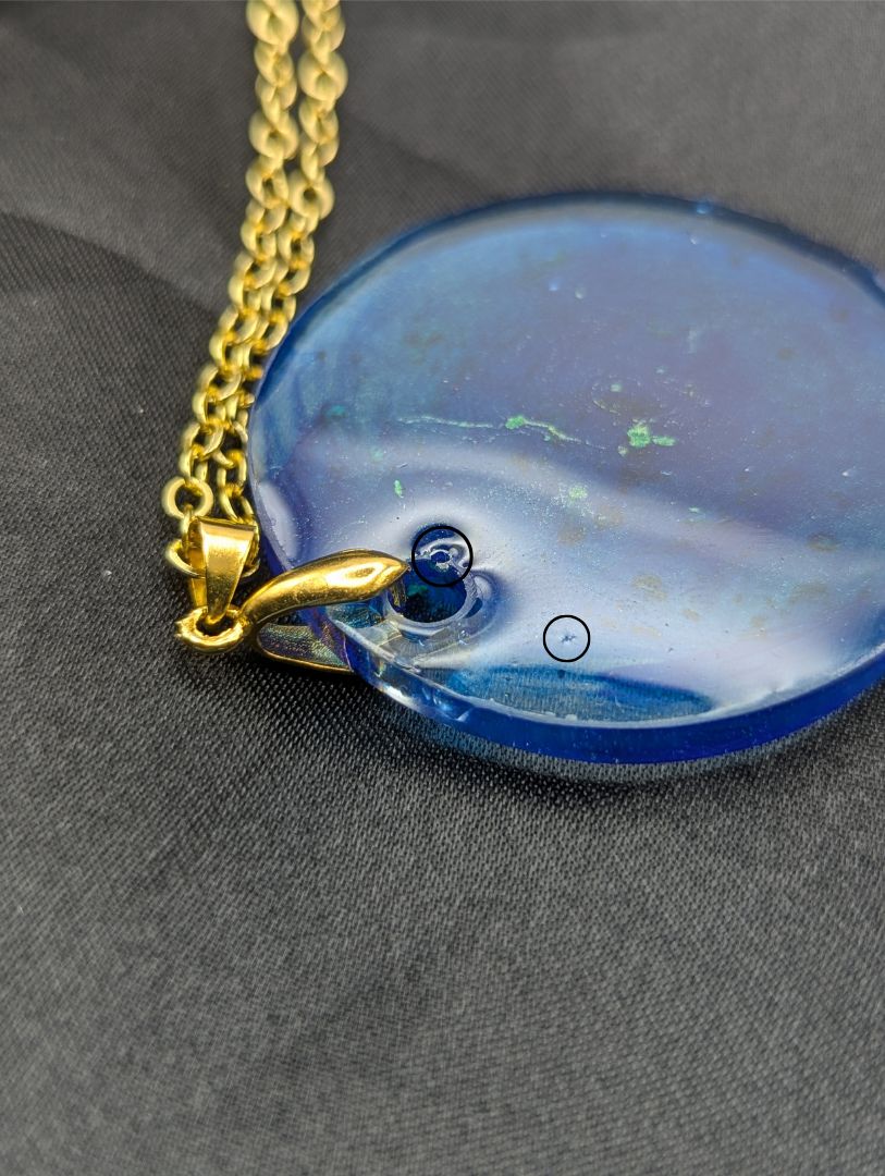 Blue resin circle pendant with speckles & swirls of green pigment powder. Resin necklace on a gold pinch bail and gold plated metal chain.