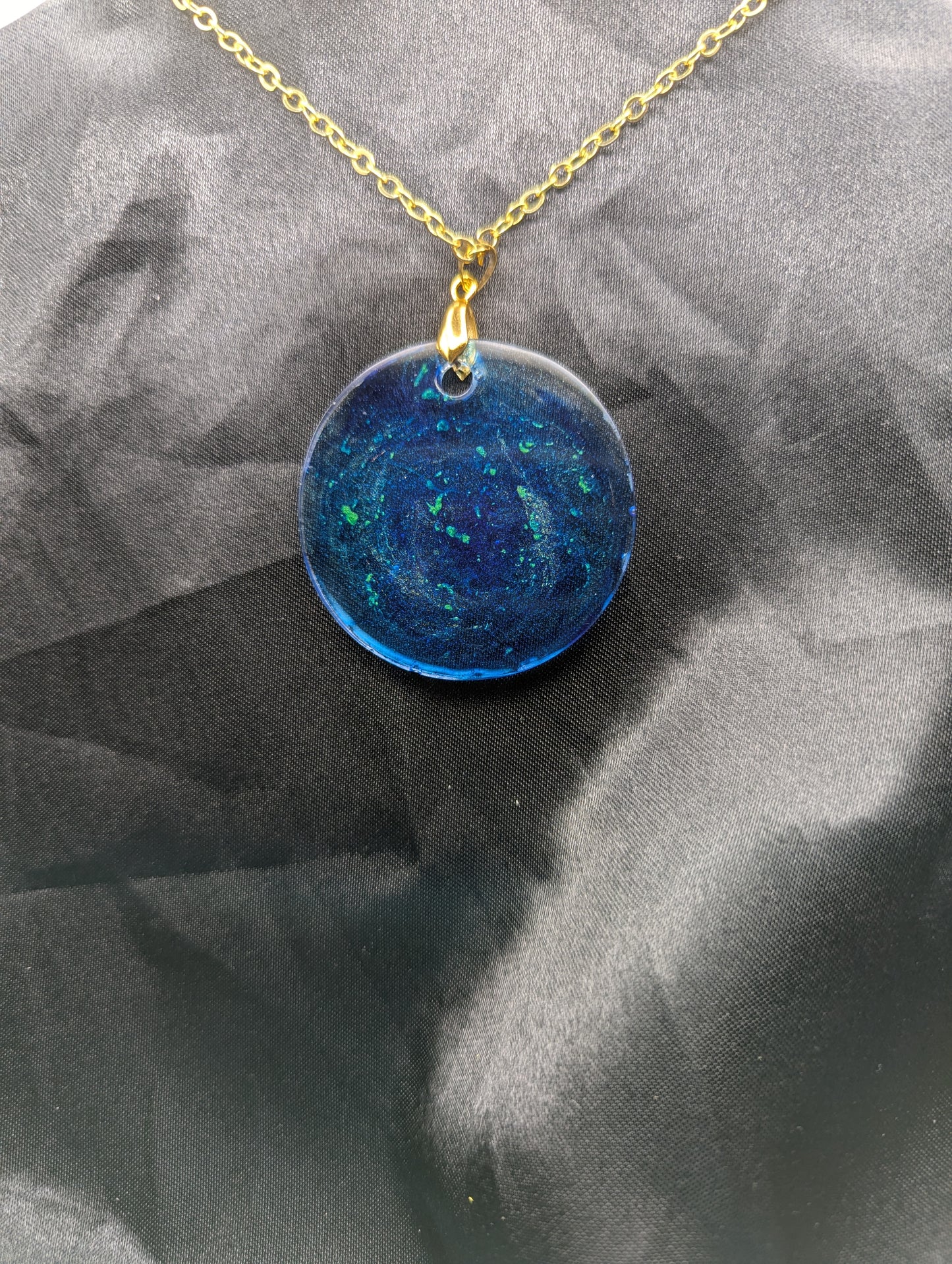 Back view of Blue resin circle pendant with speckles & swirls of green pigment powder. Resin necklace on a gold pinch bail and gold plated metal chain.