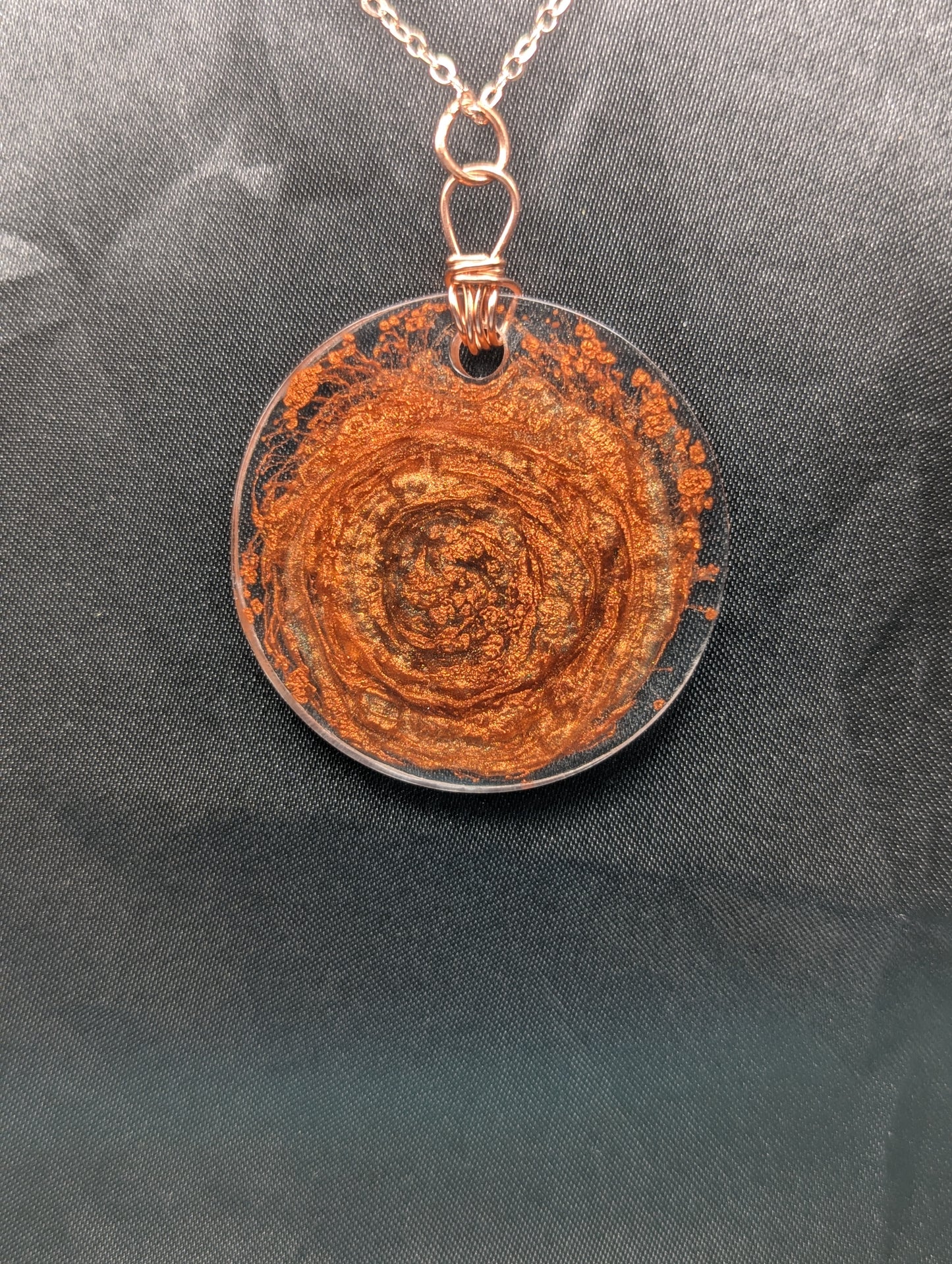 Back view of Wire wrapped copper swirl circle pendant necklace. Resin pendant with a pure copper wire bail on a rose gold colored stainless steel plated metal chain.