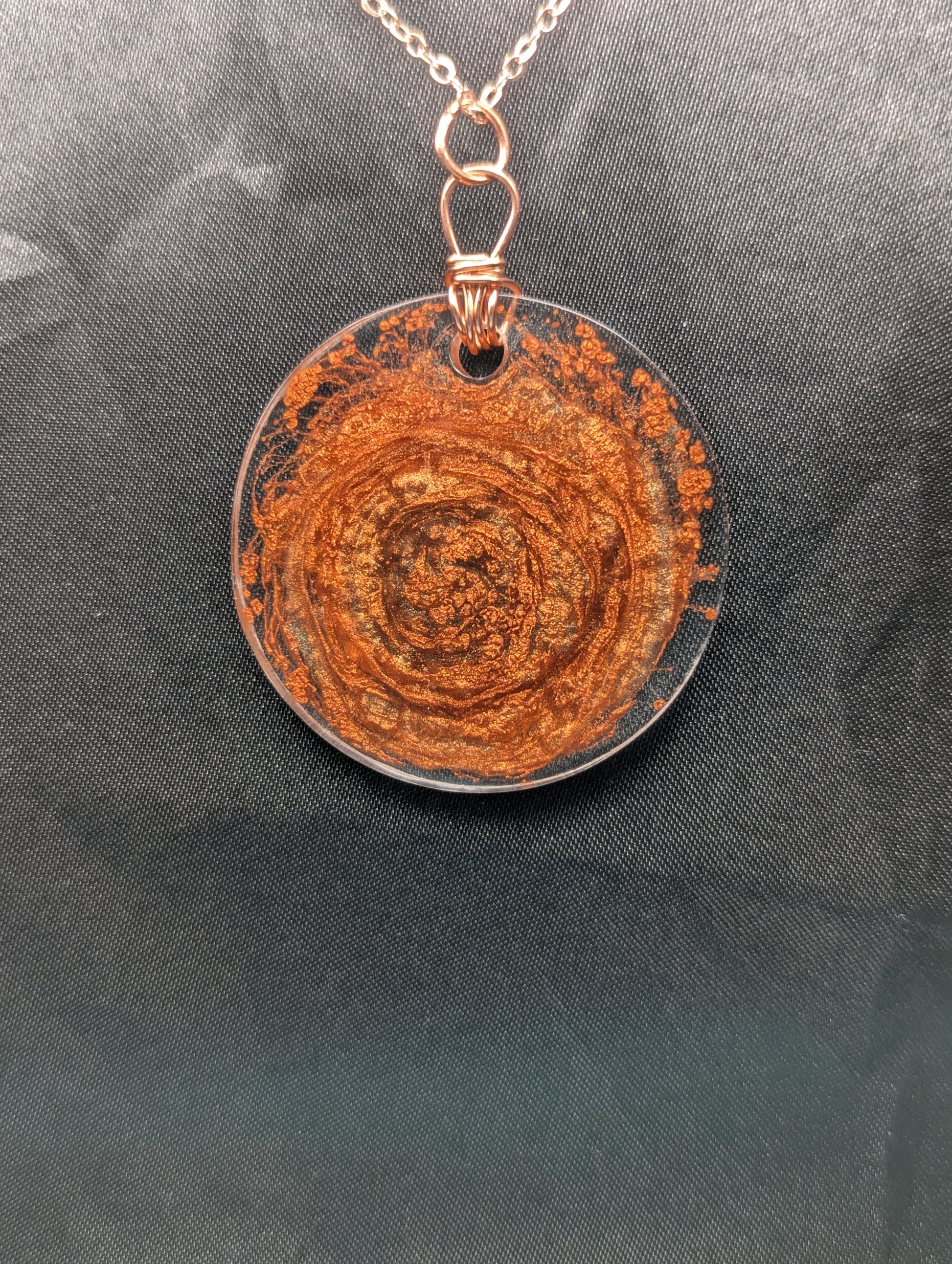 Back view of Wire wrapped copper swirl circle pendant necklace. Resin pendant with a pure copper wire bail on a rose gold colored stainless steel plated metal chain.