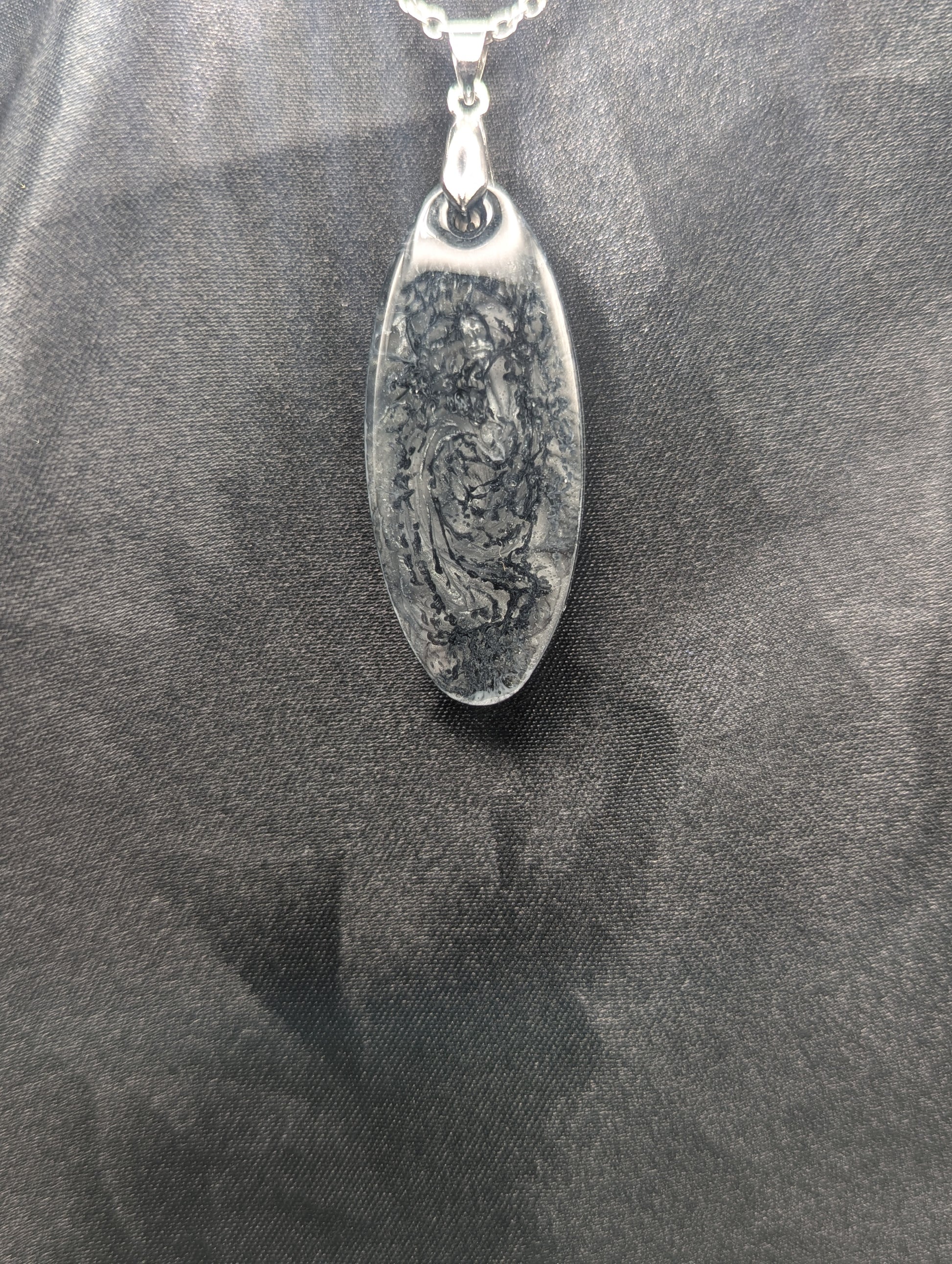 Black swirl ellipse resin pendant necklace with a white background. Resin necklace on a silver pinch bail & stainless steel chain.