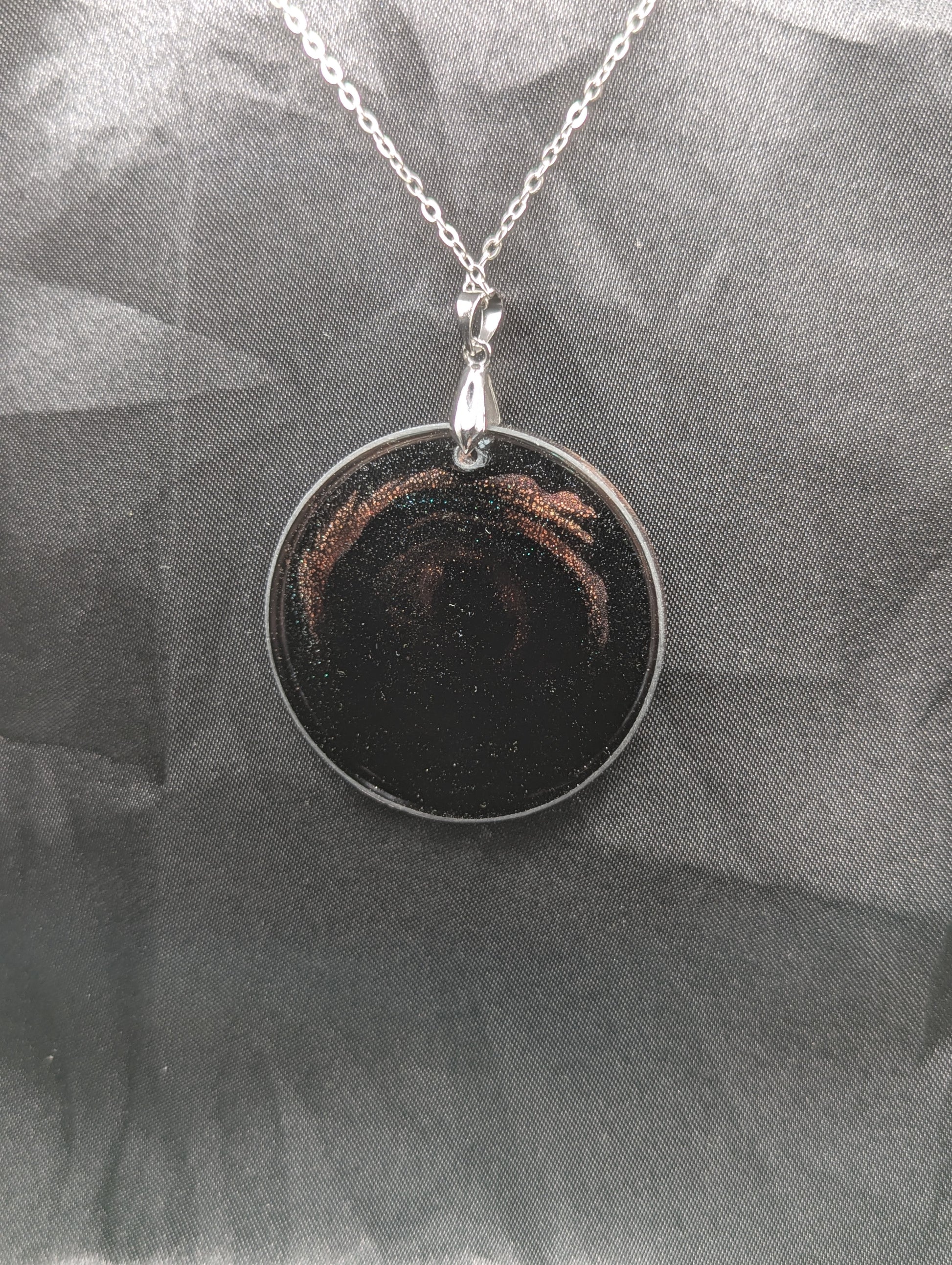 Back view of Black Resin Circle Pendant with coral-pink colored sparkly swirls inside on a silver pinch bail & stainless steel chain.