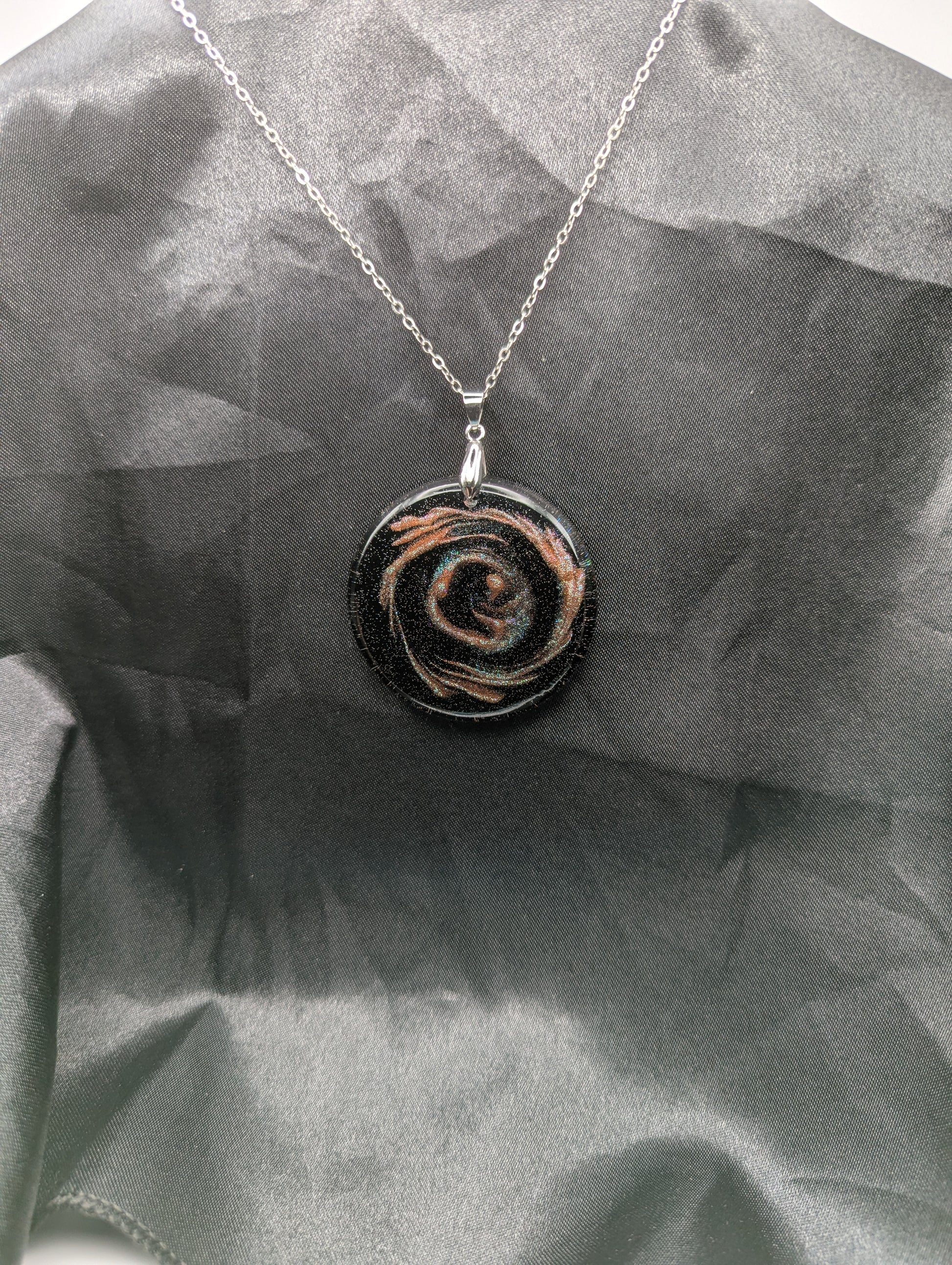 Black Resin Circle Pendant with coral-pink colored sparkly swirls inside on a silver pinch bail & stainless steel chain.
