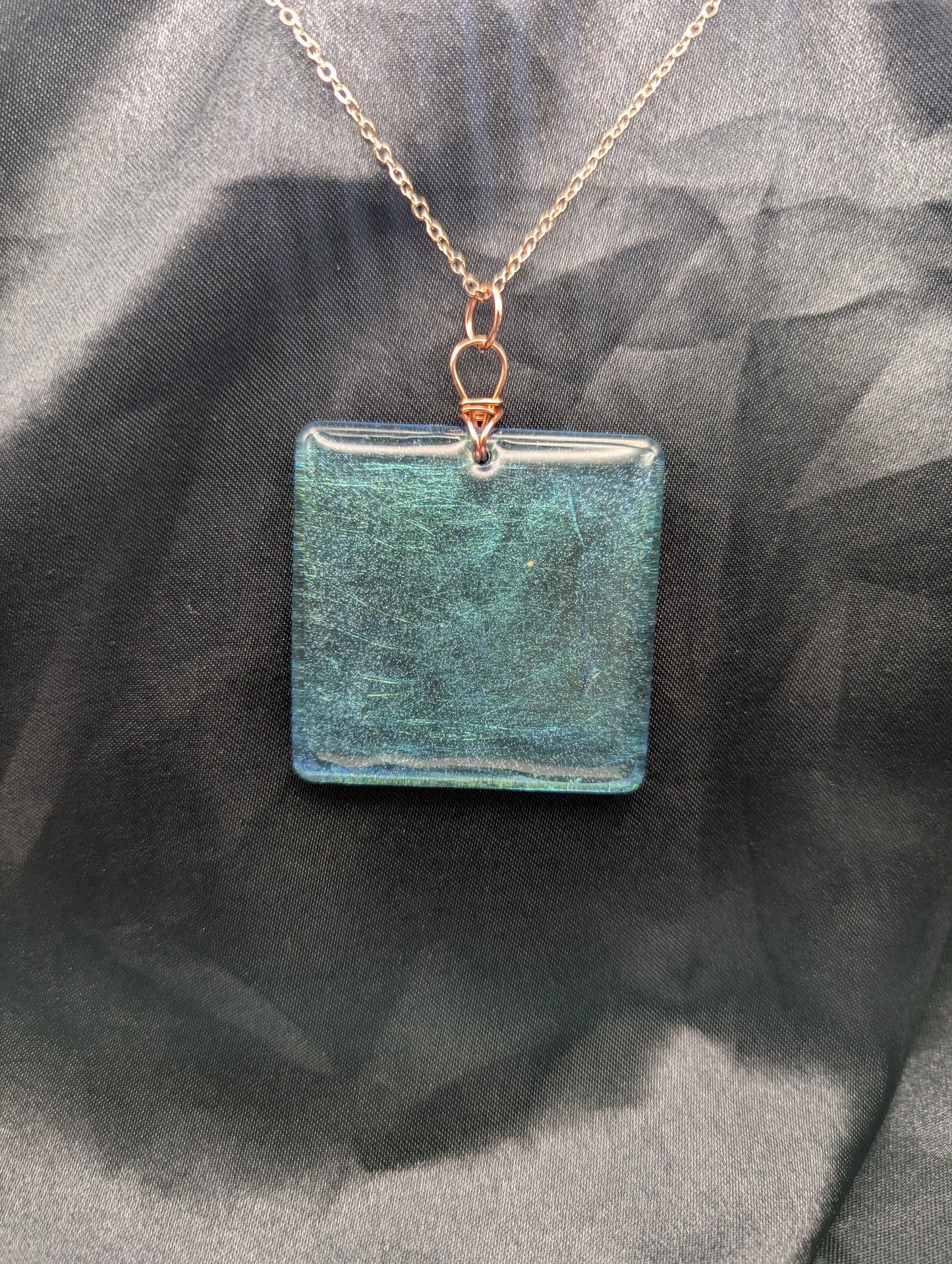 Blue square resin pendant with a color shift background. Resin pendant necklace on a pure copper wire wrapped bail & rose gold colored stainless steel plated metal chain.
