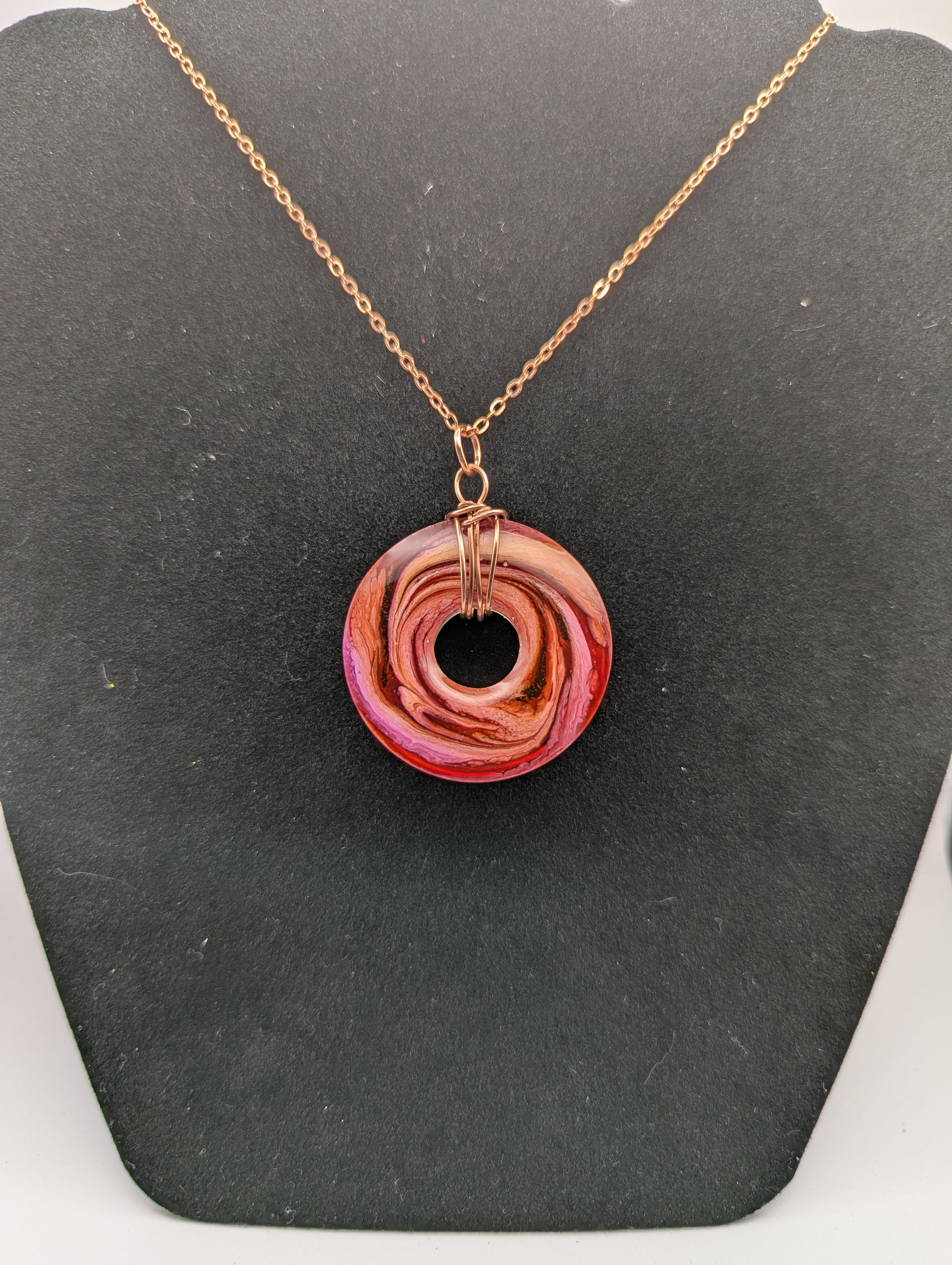 Back view of Wire Wrapped Donut Resin Pendant Necklace - Petri Effect with shades of orange, pink, & red swirls. Resin Necklace on a rose gold colored stainless steel plated metal chain.
