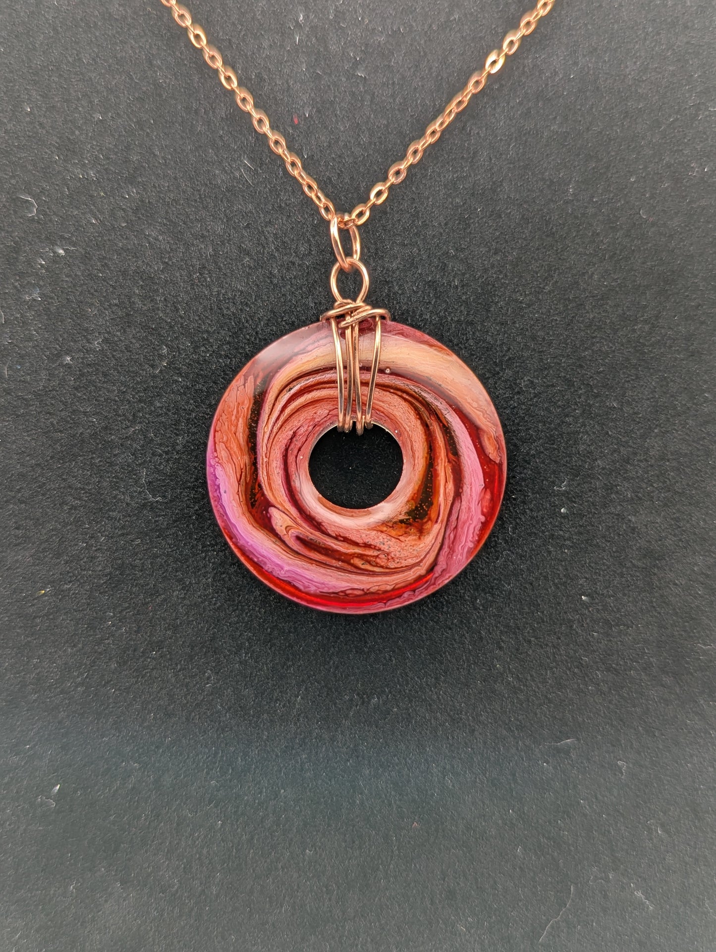 Back view of Wire Wrapped Donut Resin Pendant Necklace - Petri Effect with shades of orange, pink, & red swirls. Resin Necklace on a rose gold colored stainless steel plated metal chain.