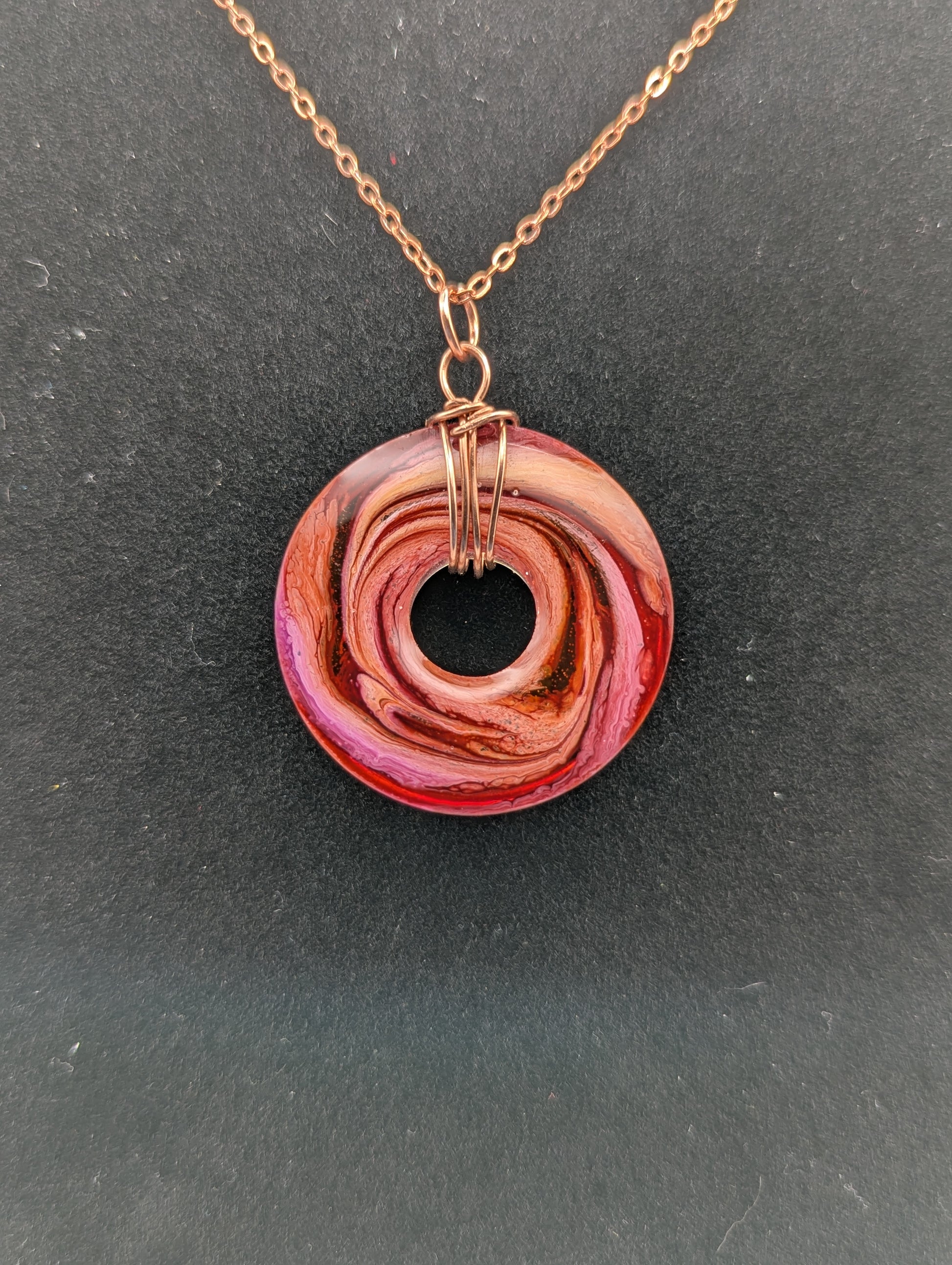 Back view of Wire Wrapped Donut Resin Pendant Necklace - Petri Effect with shades of orange, pink, & red swirls. Resin Necklace on a rose gold colored stainless steel plated metal chain.