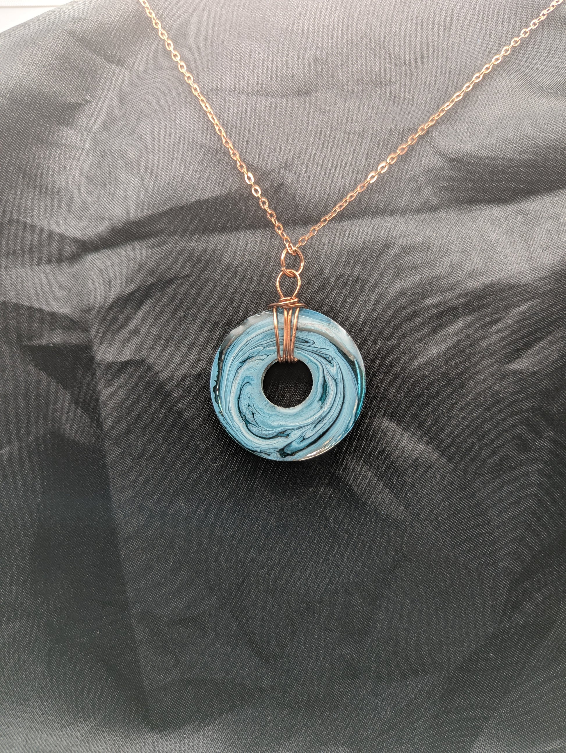 Back view of Wire Wrapped Donut Resin Pendant Necklace - Petri Effect with shades of blue & metallic bronze swirls. Resin Necklace on a rose gold colored stainless steel metal chain