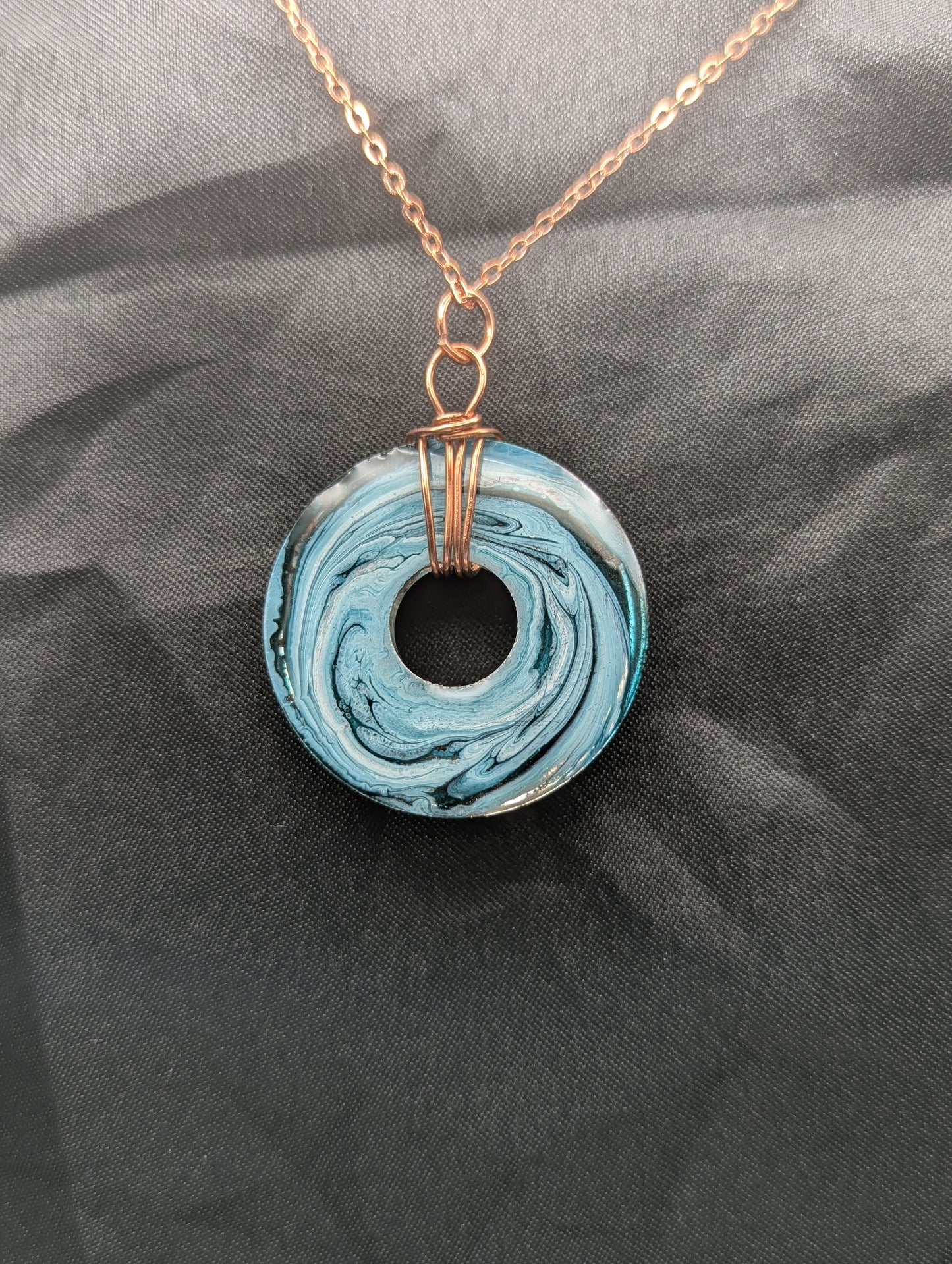 Back view of Wire Wrapped Donut Resin Pendant Necklace - Petri Effect with shades of blue & metallic bronze swirls. Resin Necklace on a rose gold colored stainless steel metal chain