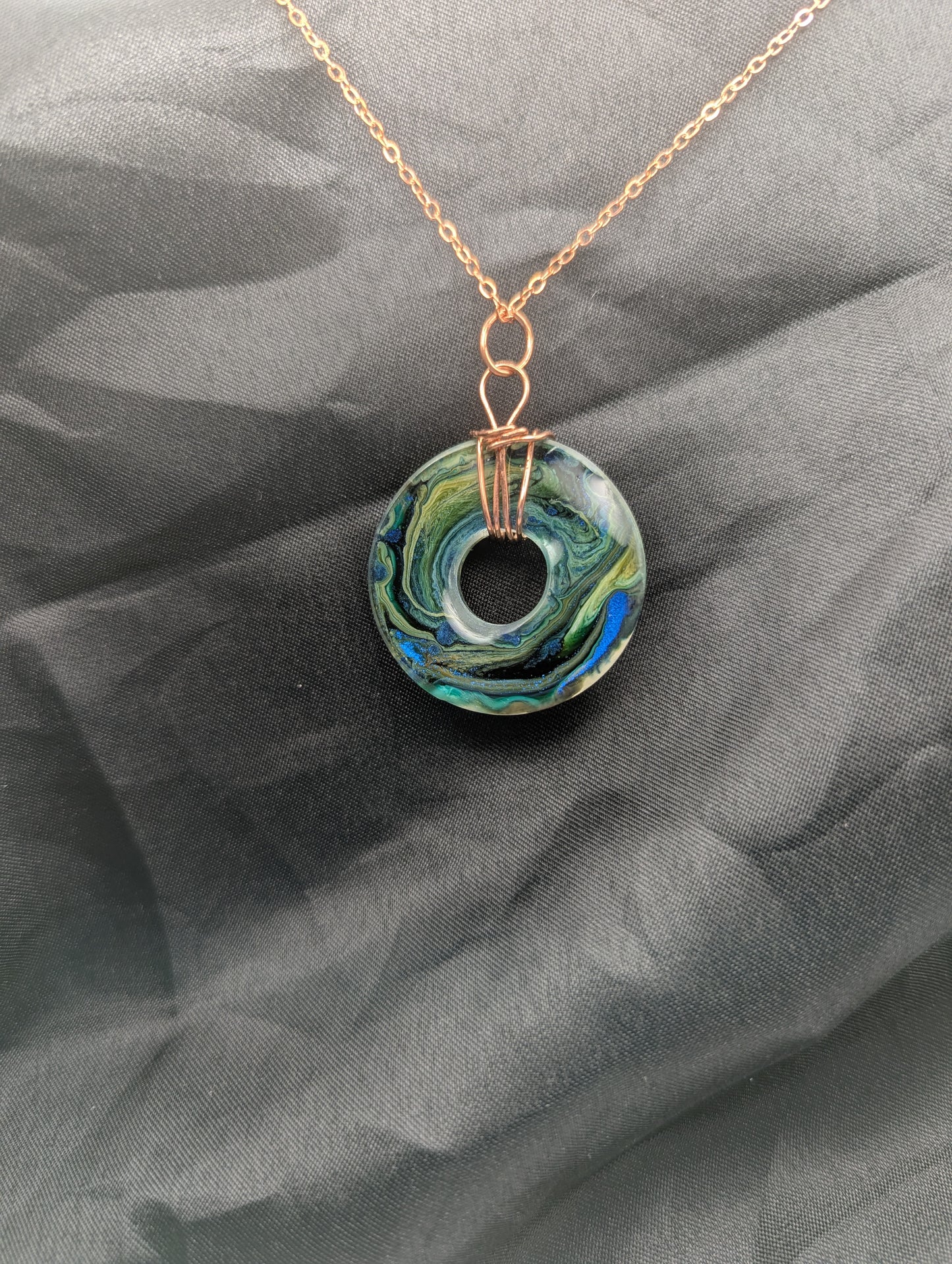 Back view of Wire Wrapped Donut Resin Pendant Necklace - Petri Effect with shades of blue, green, & yellow swirls. Resin Necklace on a rose gold colored stainless steel metal chain.