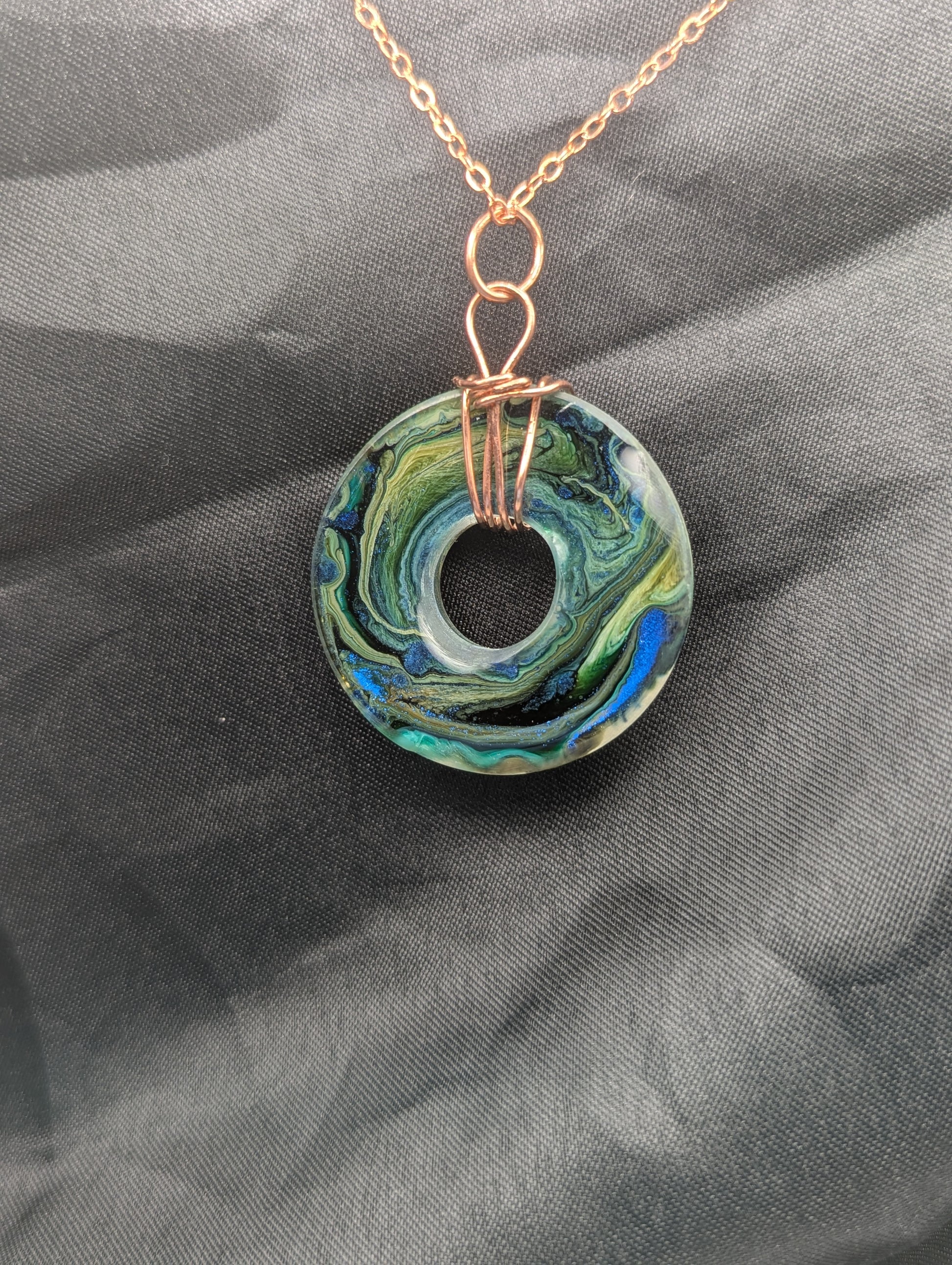 Back view of Wire Wrapped Donut Resin Pendant Necklace - Petri Effect with shades of blue, green, & yellow swirls. Resin Necklace on a rose gold colored stainless steel metal chain.