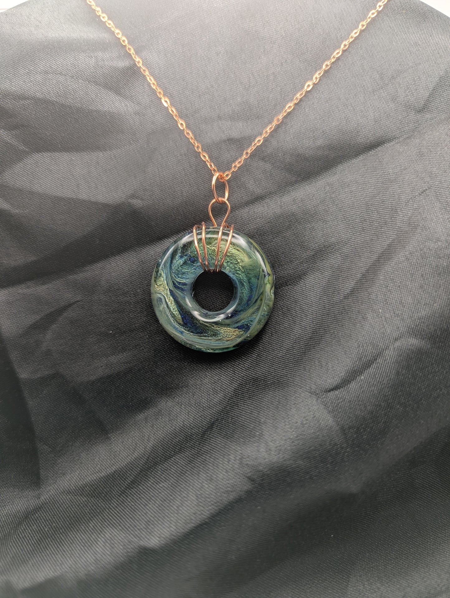 Wire Wrapped Donut Resin Pendant Necklace - Petri Effect with shades of blue, green, & yellow swirls. Resin Necklace on a rose gold colored stainless steel metal chain.