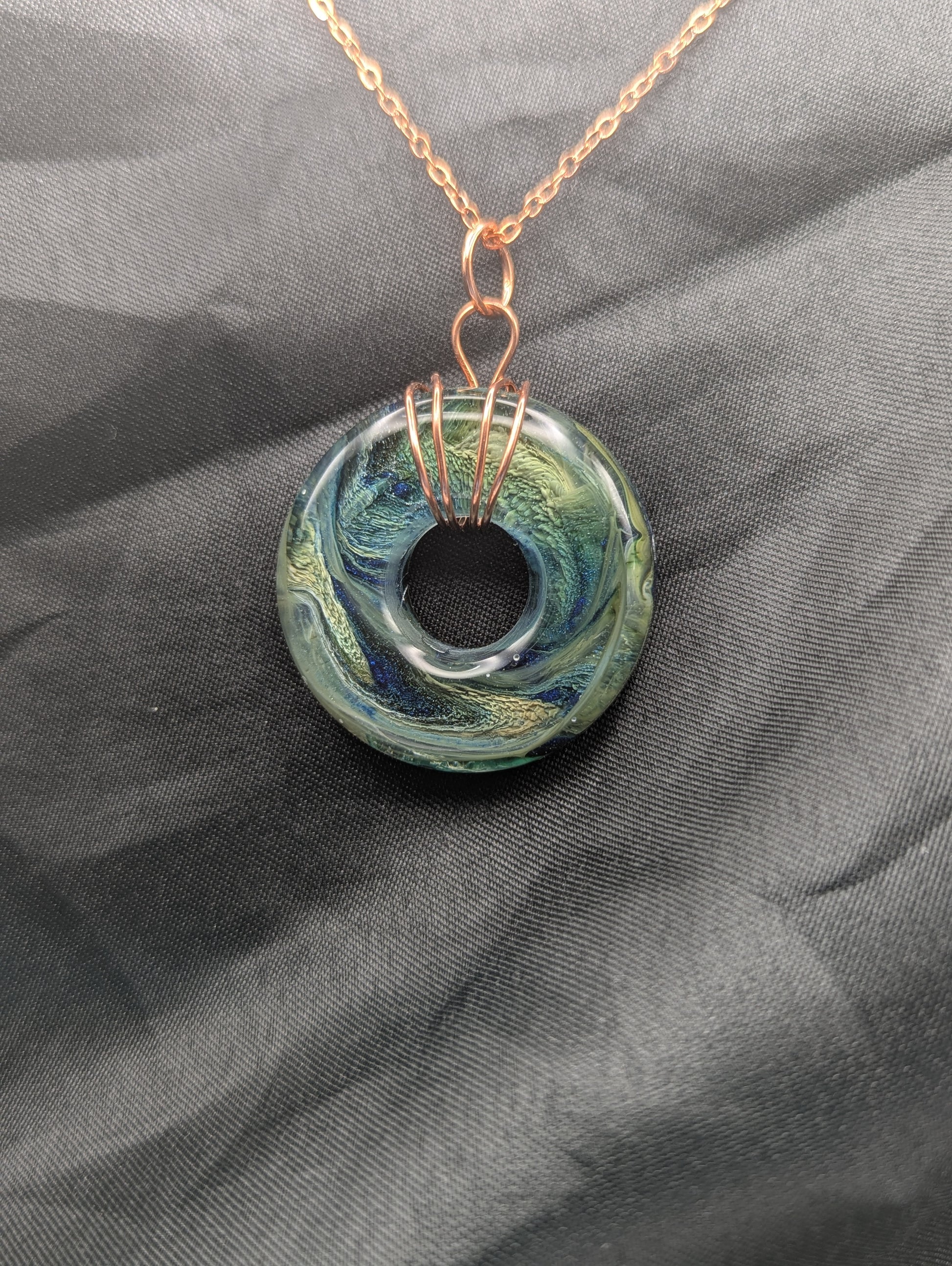 Wire Wrapped Donut Resin Pendant Necklace - Petri Effect with shades of blue, green, & yellow swirls. Resin Necklace on a rose gold colored stainless steel metal chain.