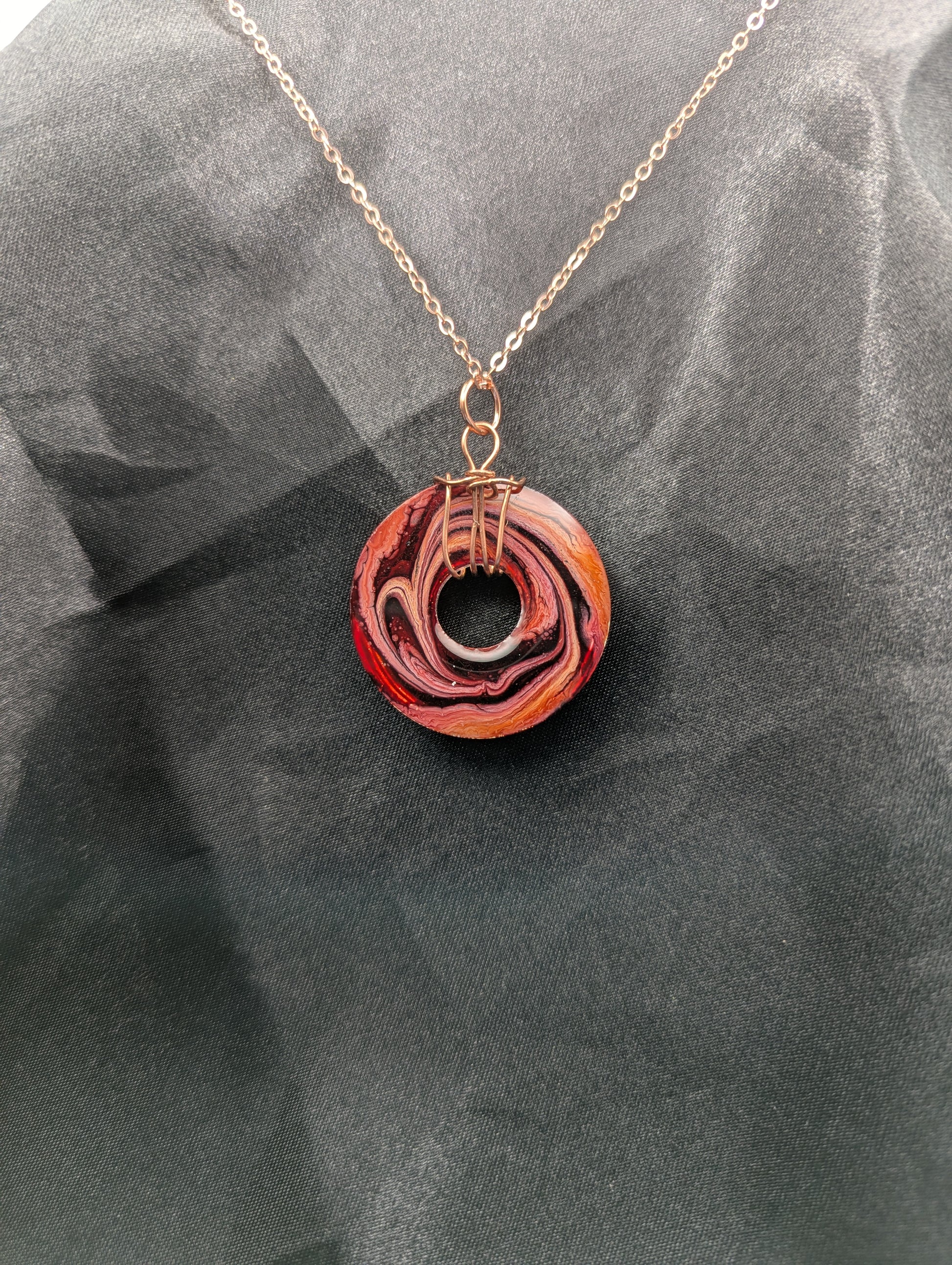 Back view of Wire Wrapped Donut Resin Pendant Necklace - Petri Effect with shades of red, pink, & orange swirls. Resin Necklace on a rose gold colored stainless steel plated metal chain.
