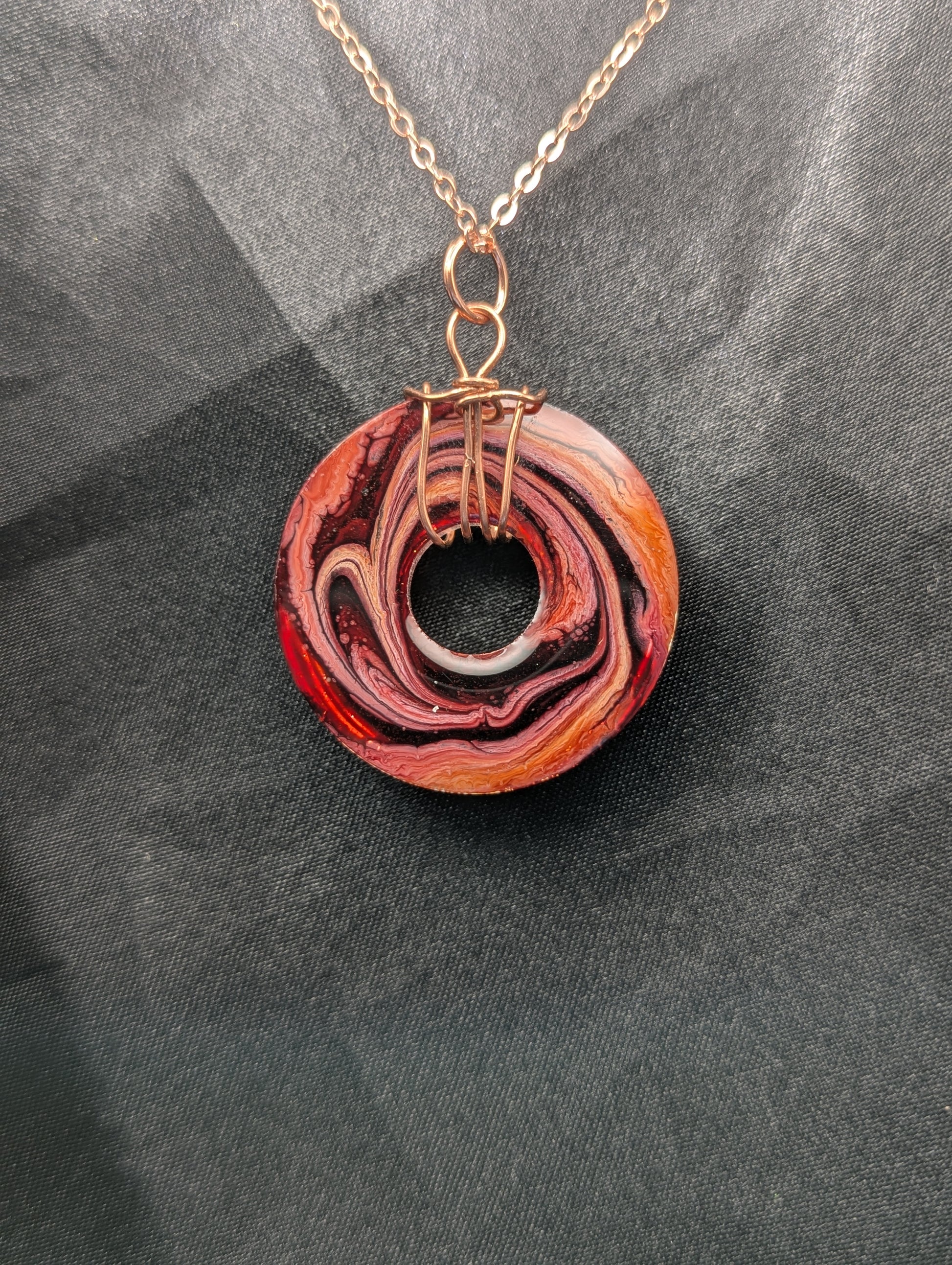 Back view of Wire Wrapped Donut Resin Pendant Necklace - Petri Effect with shades of red, pink, & orange swirls. Resin Necklace on a rose gold colored stainless steel plated metal chain.