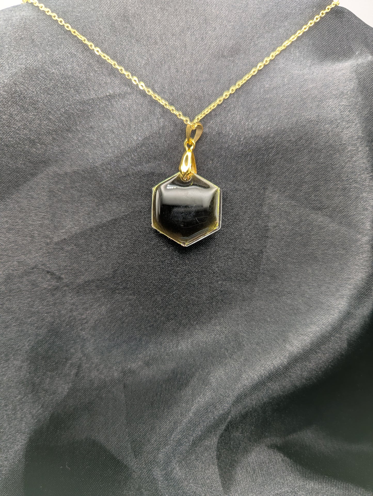 Back view of Yellow Hexagon Pendant Necklace with a color shifting background. Resin pendant on a gold pinch bail & gold plated metal chain.