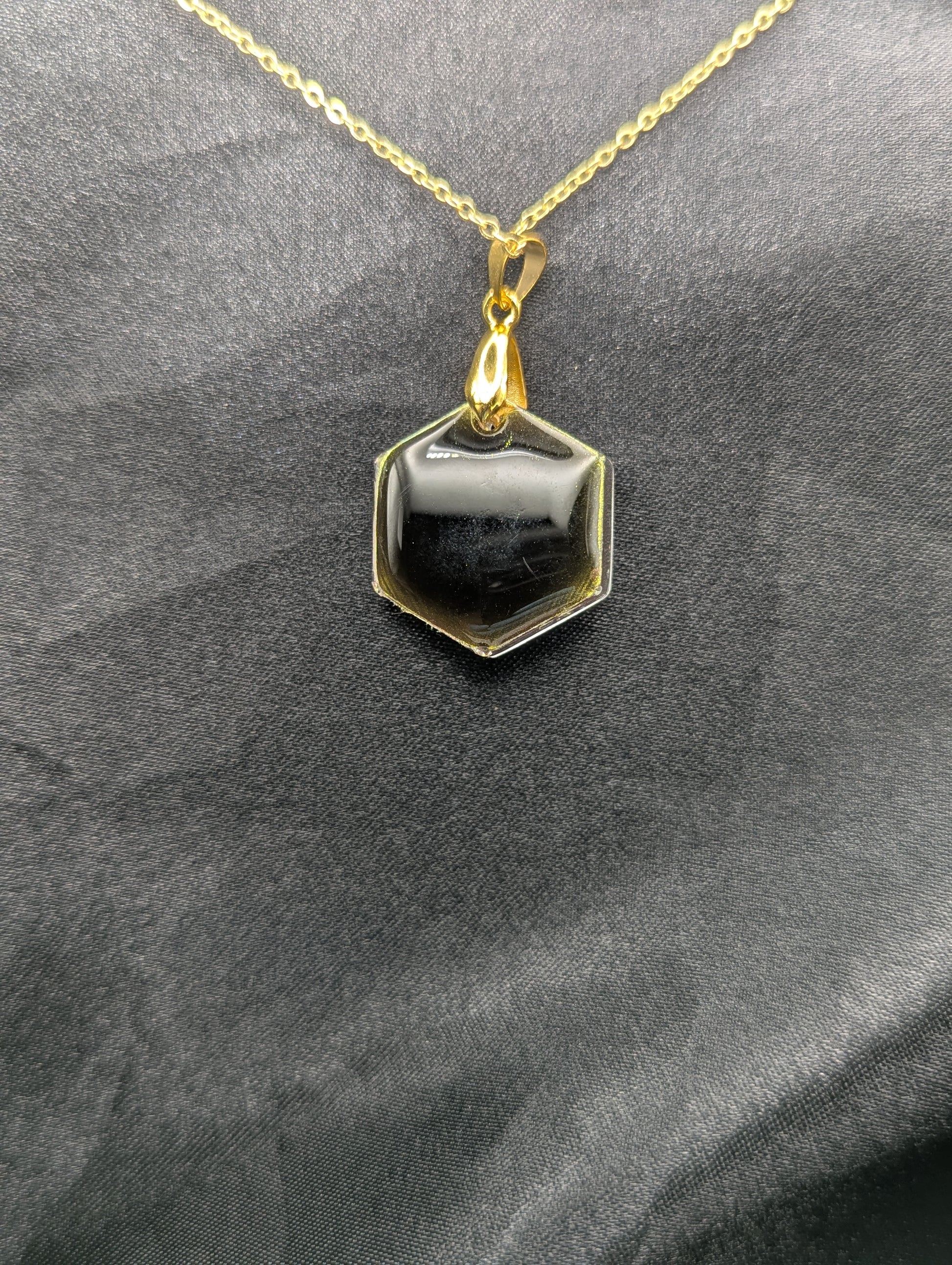 Back view of Yellow Hexagon Pendant Necklace with a color shifting background. Resin pendant on a gold pinch bail & gold plated metal chain.