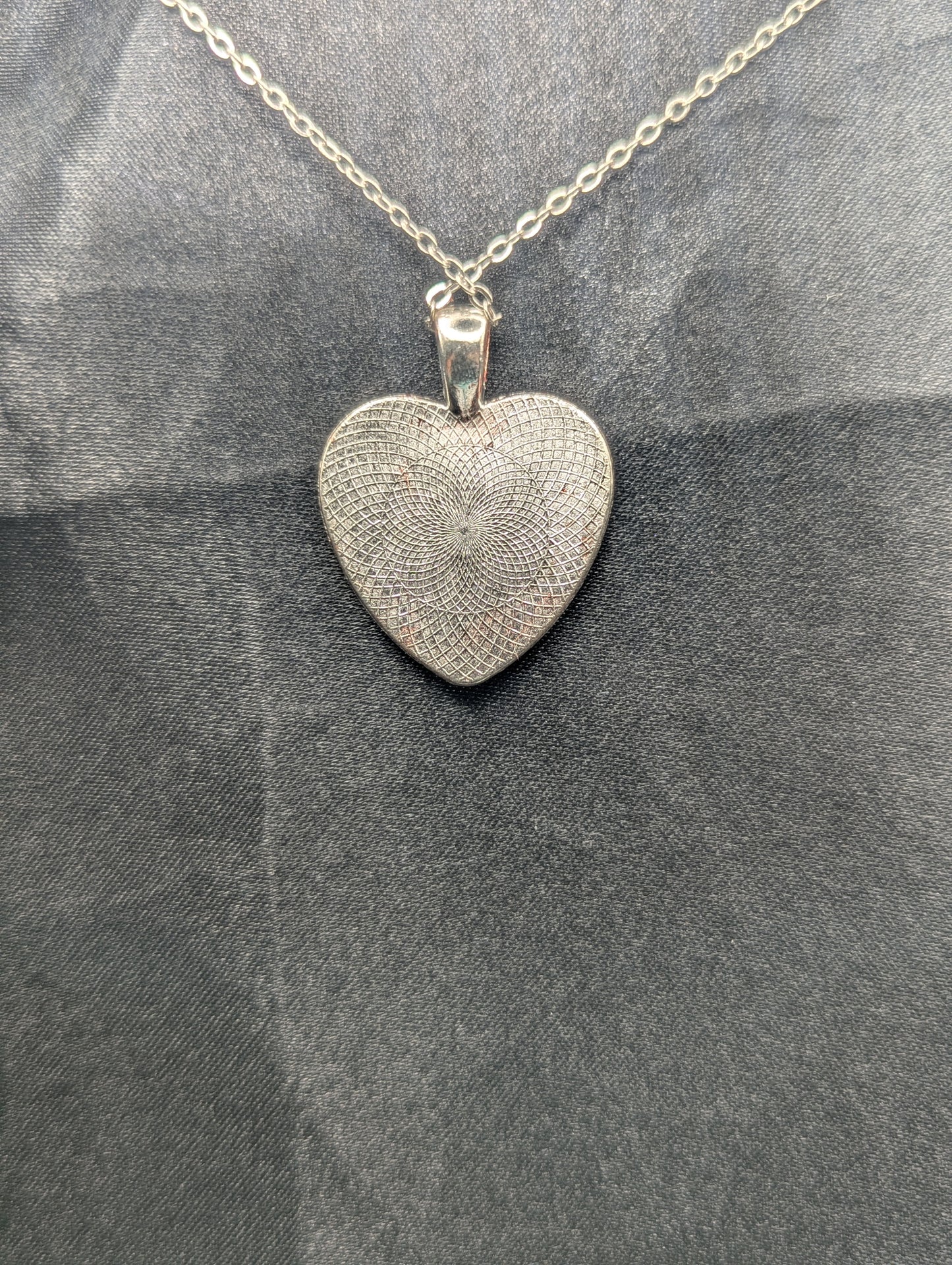 Back view of Silver colored heart shaped metal bezel filled with a transparent sparkly red resin. Resin pendant necklace on a stainless steel chain.