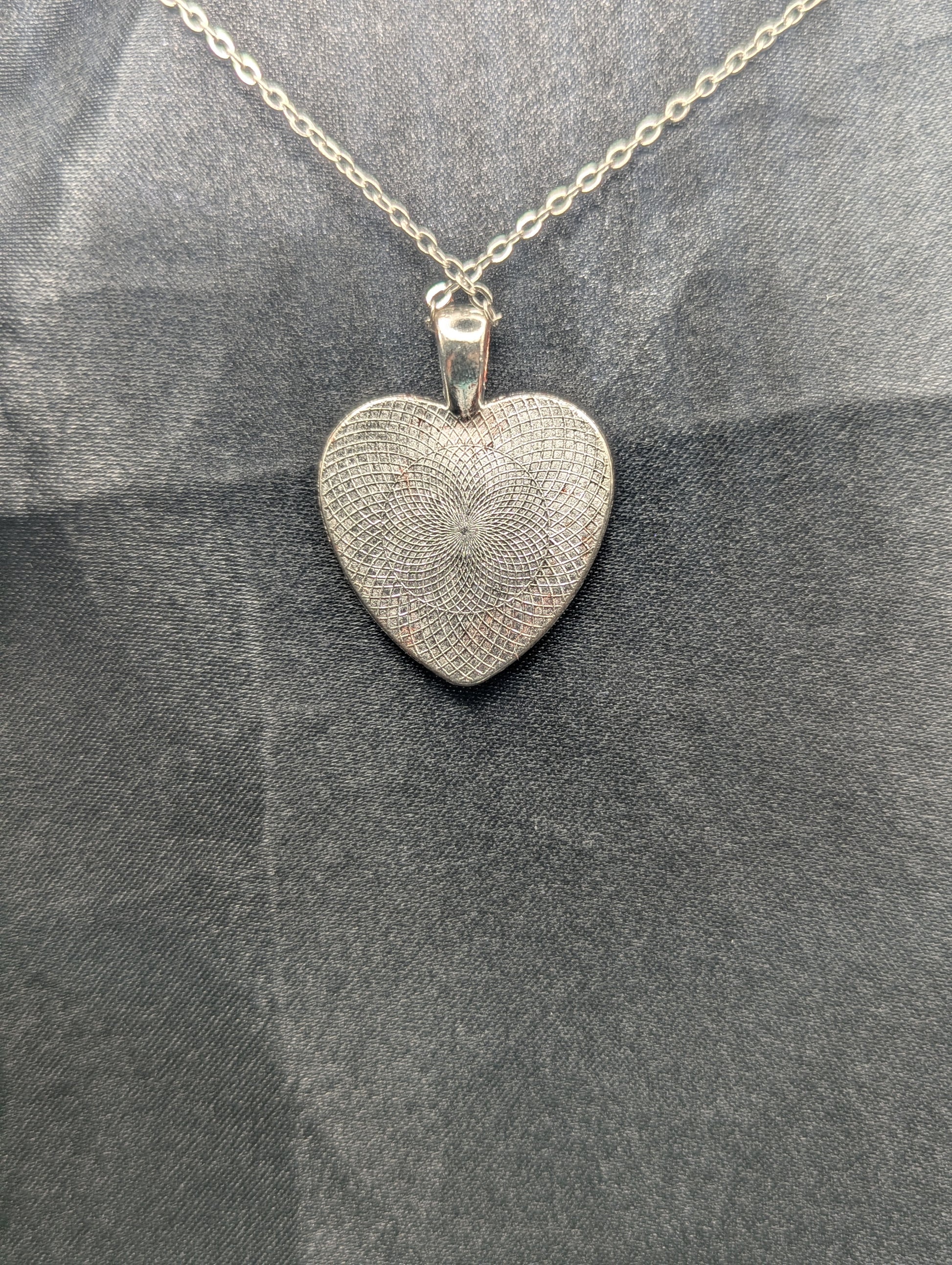 Back view of Silver colored heart shaped metal bezel filled with a transparent sparkly red resin. Resin pendant necklace on a stainless steel chain.