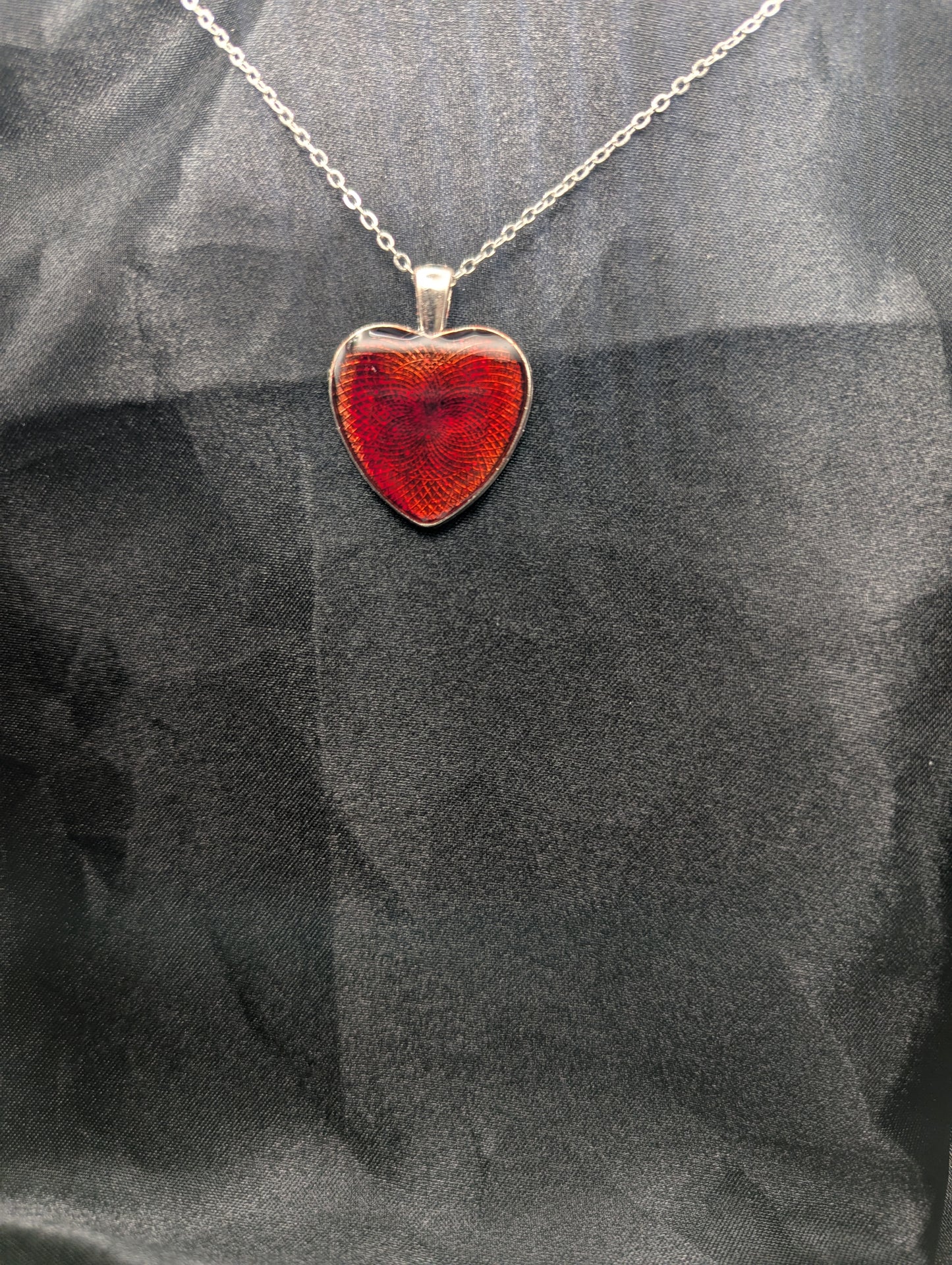 Silver colored heart shaped metal bezel filled with a transparent sparkly red resin. Resin pendant necklace on a stainless steel chain.