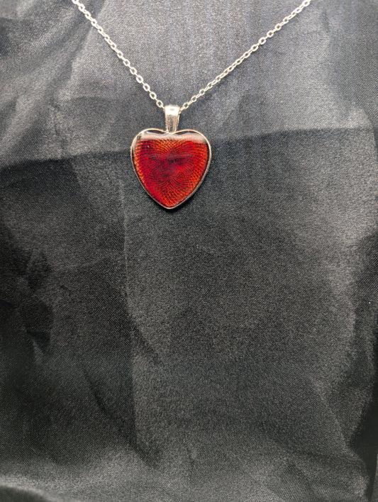Silver colored heart shaped metal bezel filled with a transparent sparkly red resin. Resin pendant necklace on a stainless steel chain.