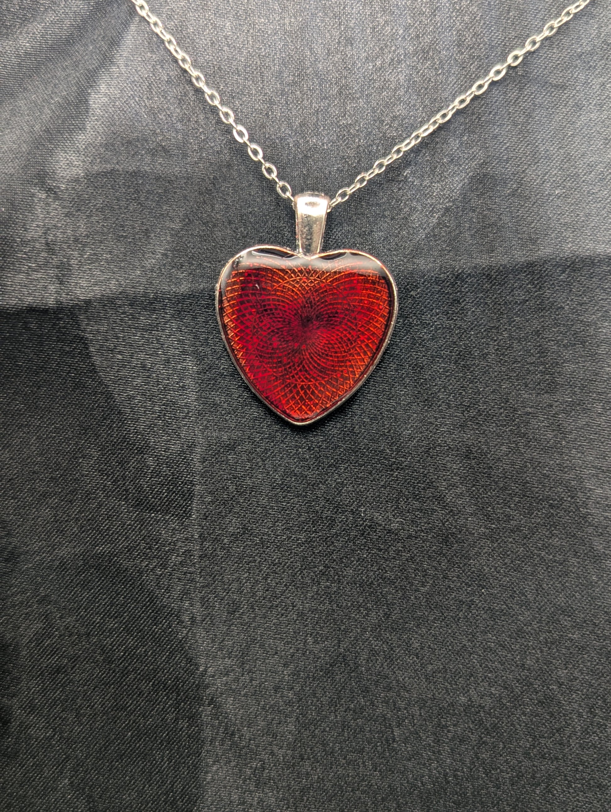 Silver colored heart shaped metal bezel filled with a transparent sparkly red resin. Resin pendant necklace on a stainless steel chain.