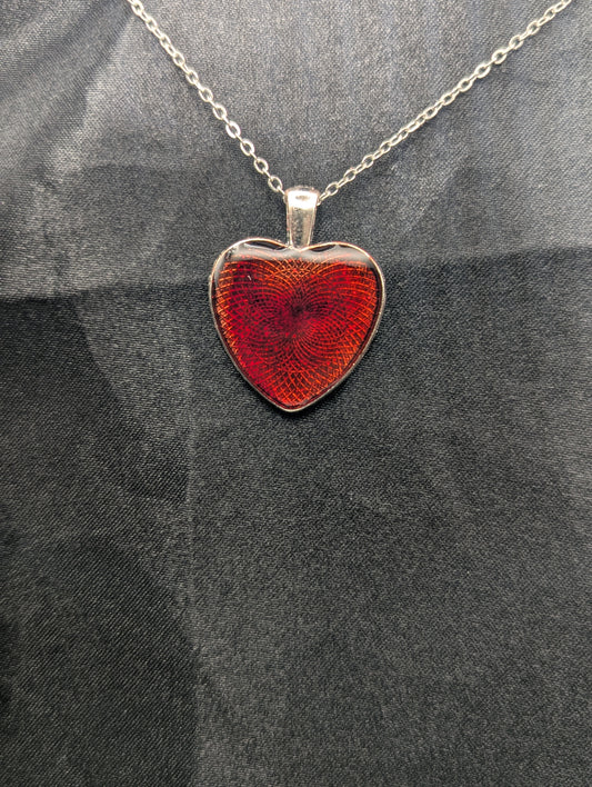 Silver colored heart shaped metal bezel filled with a transparent sparkly red resin. Resin pendant necklace on a stainless steel chain.