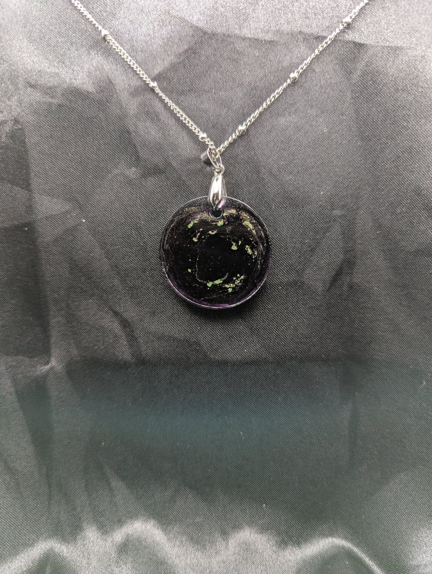 Back view of Deep purple circle resin pendant with speckles of green pigment on a silver pinch bail and stainless steel chain