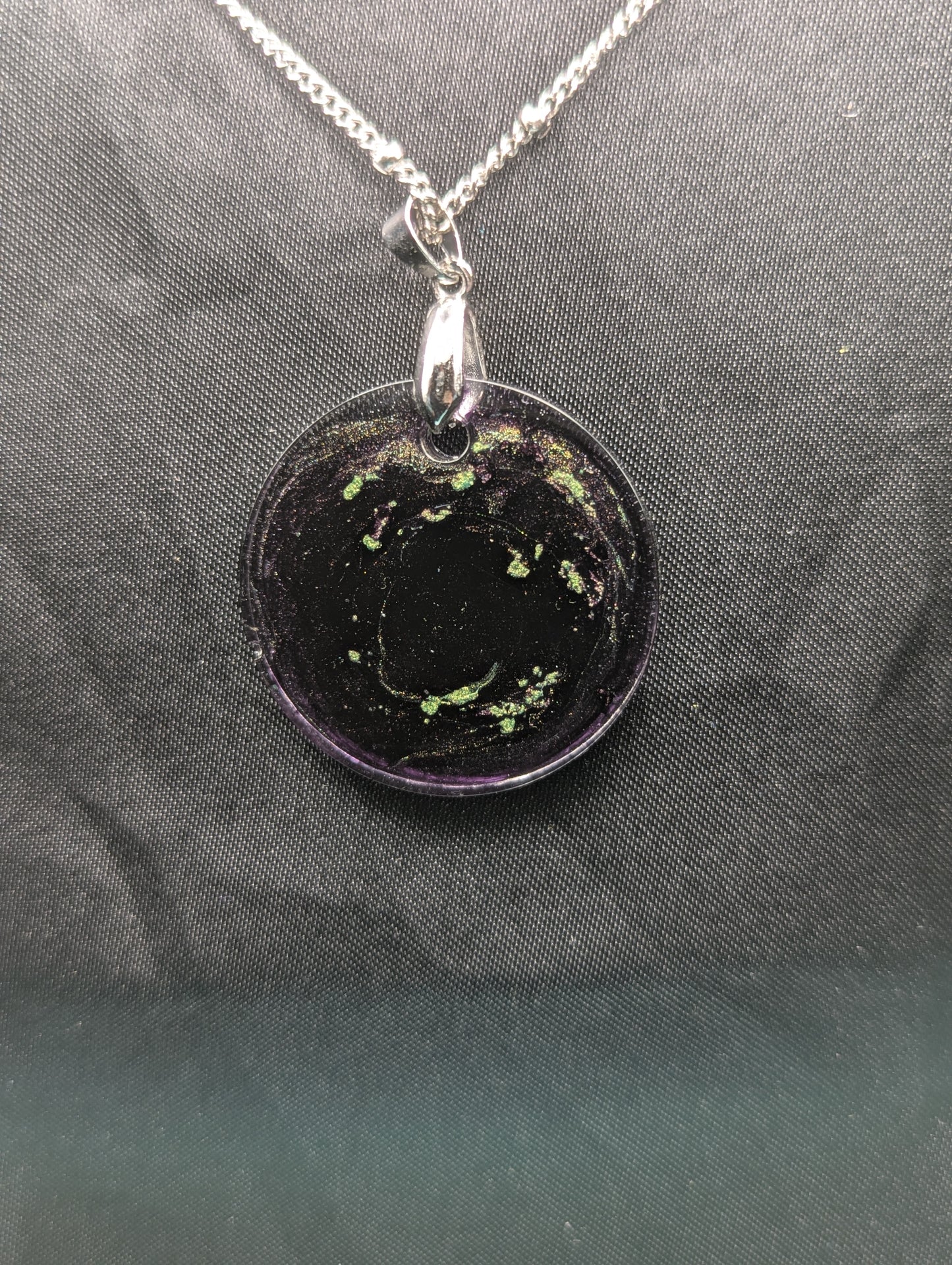 Back view of Deep purple circle resin pendant with speckles of green pigment on a silver pinch bail and stainless steel chain