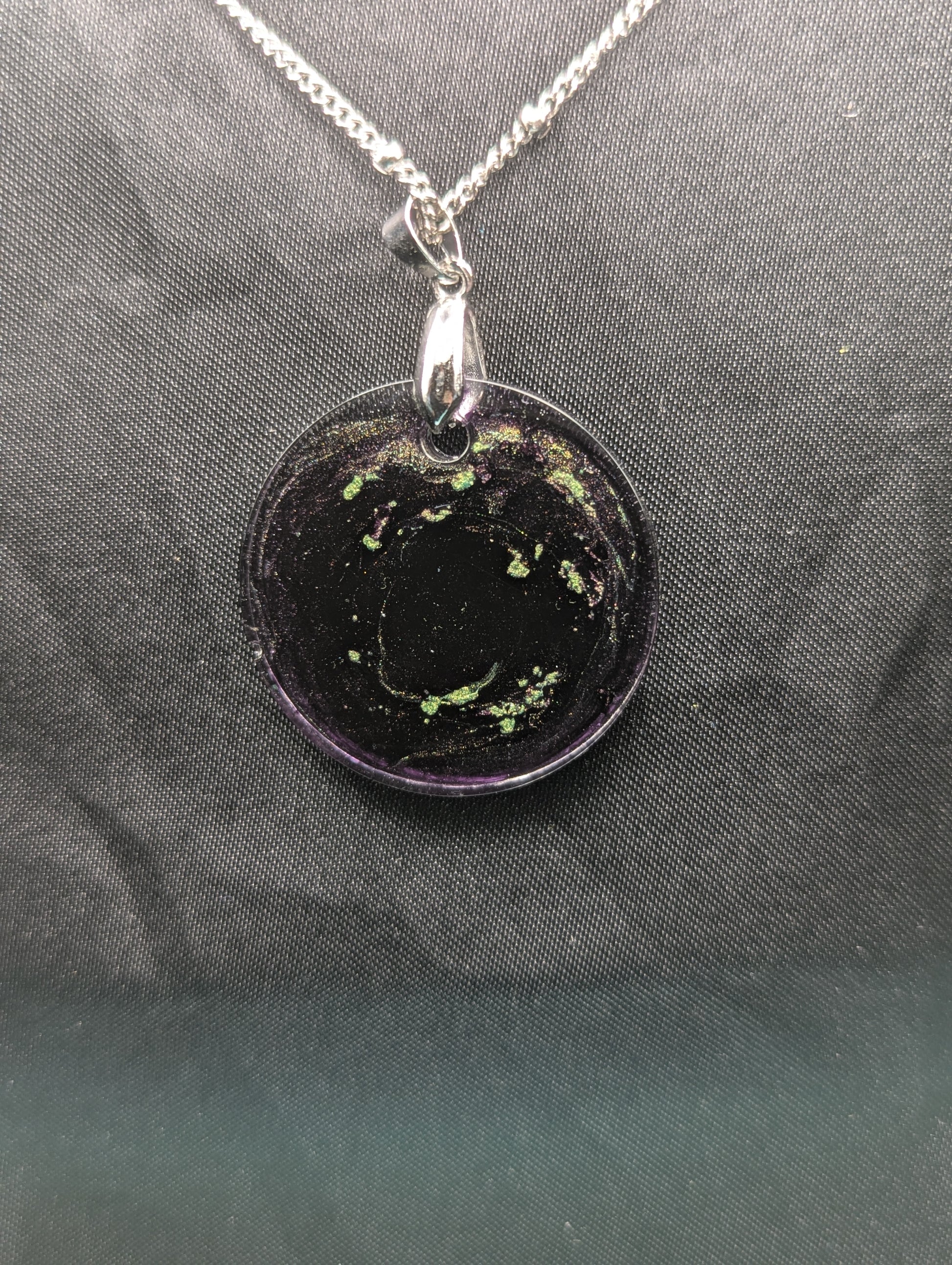 Back view of Deep purple circle resin pendant with speckles of green pigment on a silver pinch bail and stainless steel chain