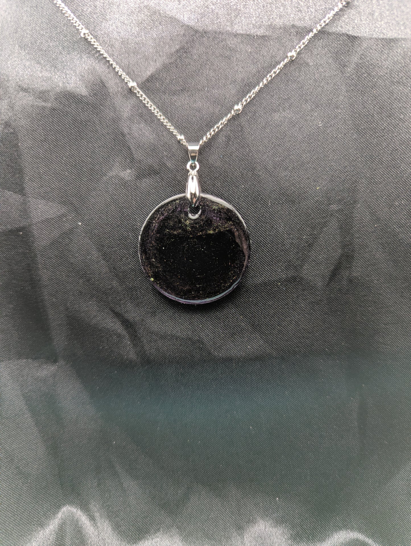 Deep purple circle resin pendant with speckles of green pigment on a silver pinch bail and stainless steel chain