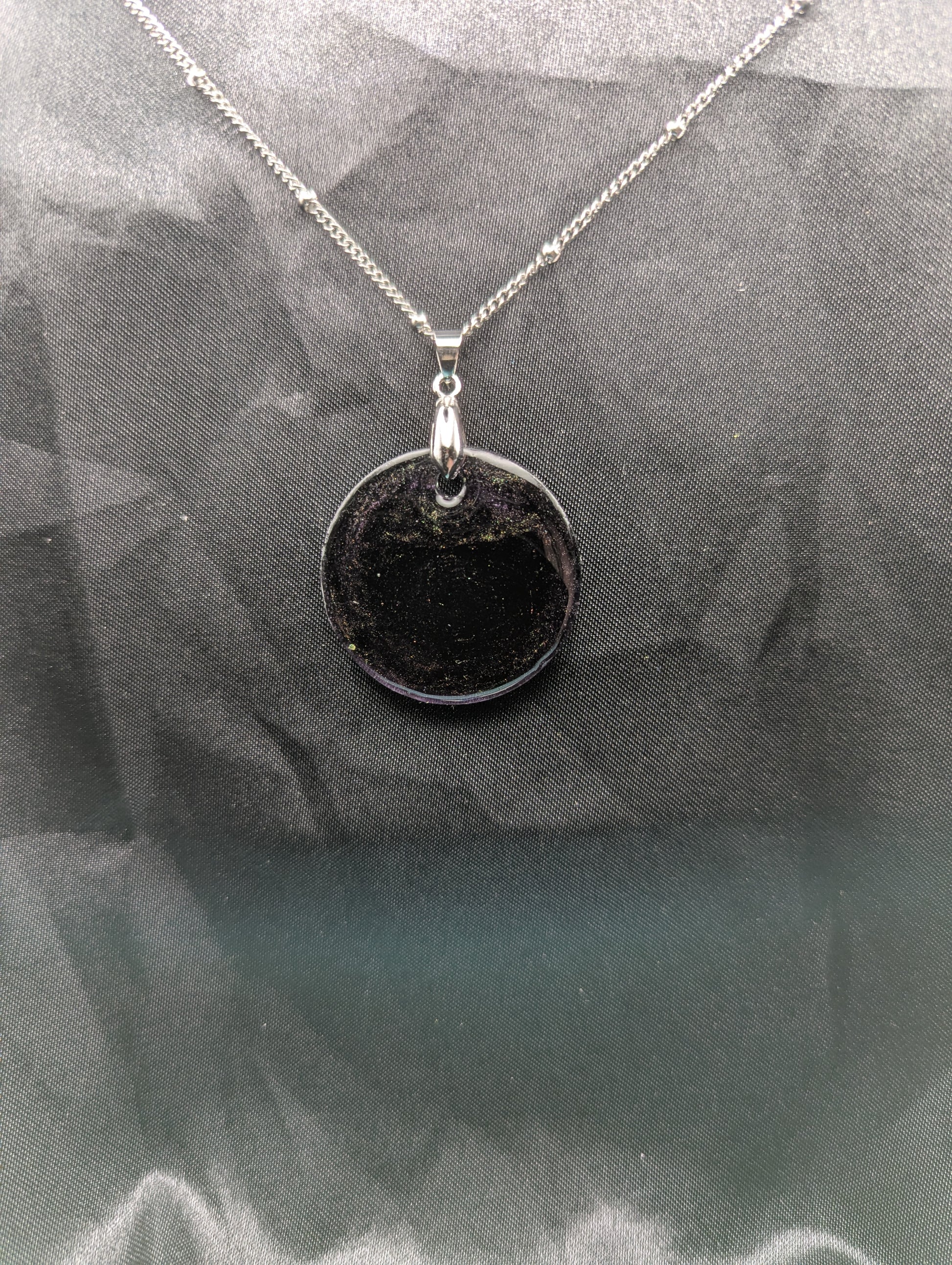 Deep purple circle resin pendant with speckles of green pigment on a silver pinch bail and stainless steel chain