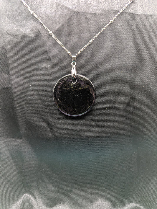 Deep purple circle resin pendant with speckles of green pigment on a silver pinch bail and stainless steel chain