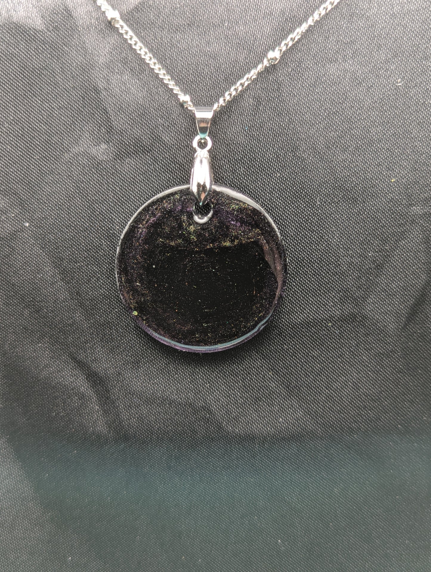 Deep purple circle resin pendant with speckles of green pigment on a silver pinch bail and stainless steel chain