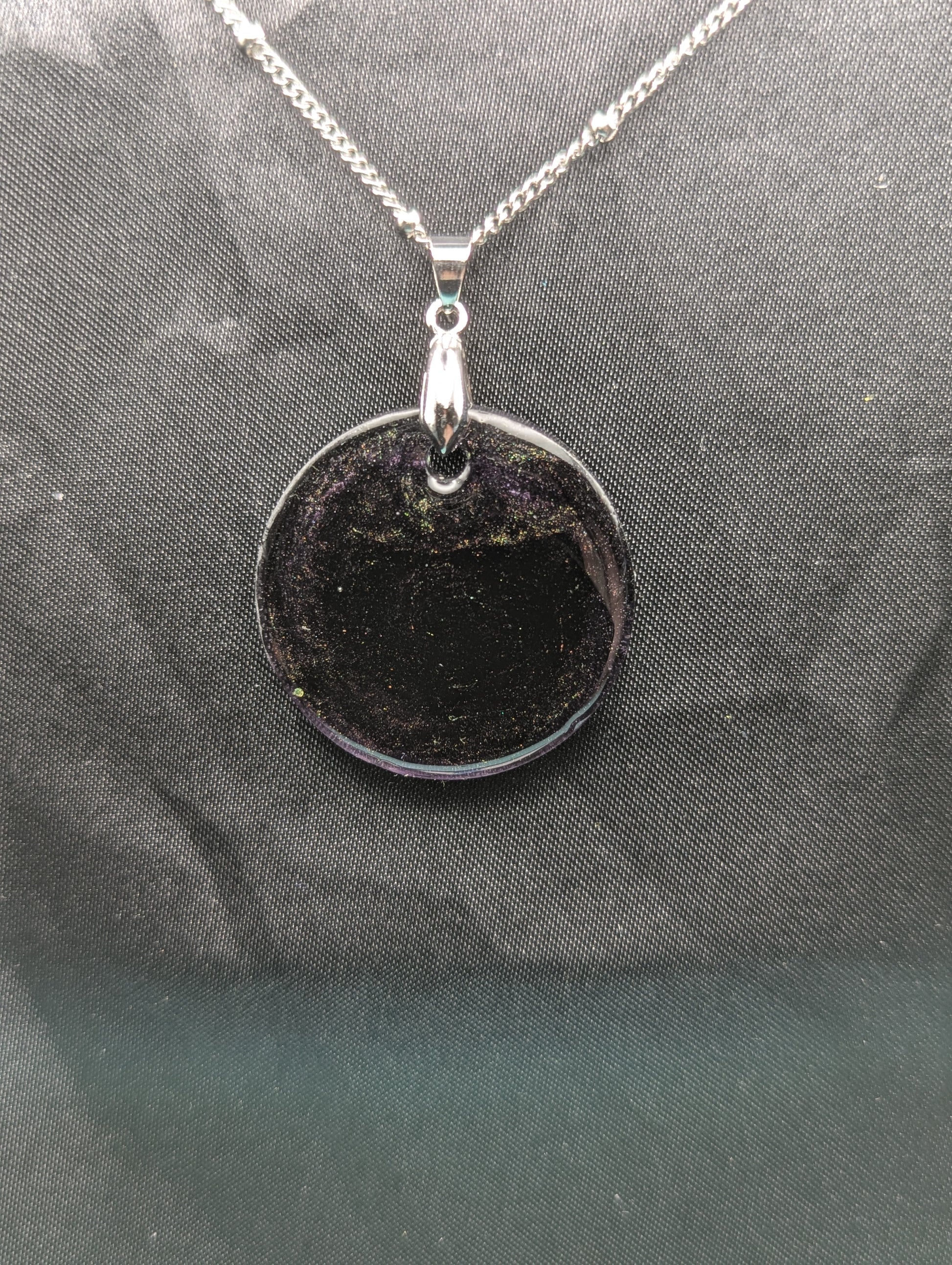 Deep purple circle resin pendant with speckles of green pigment on a silver pinch bail and stainless steel chain