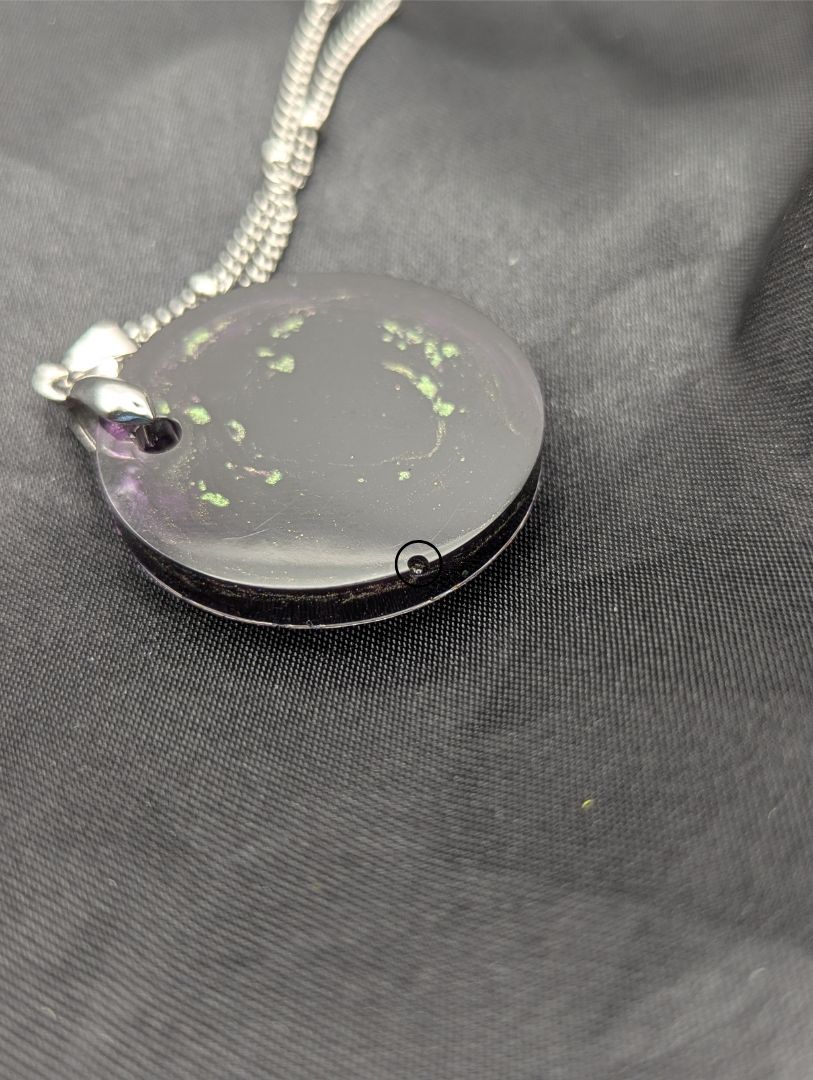 Deep purple circle resin pendant with speckles of green pigment on a silver pinch bail and stainless steel chain