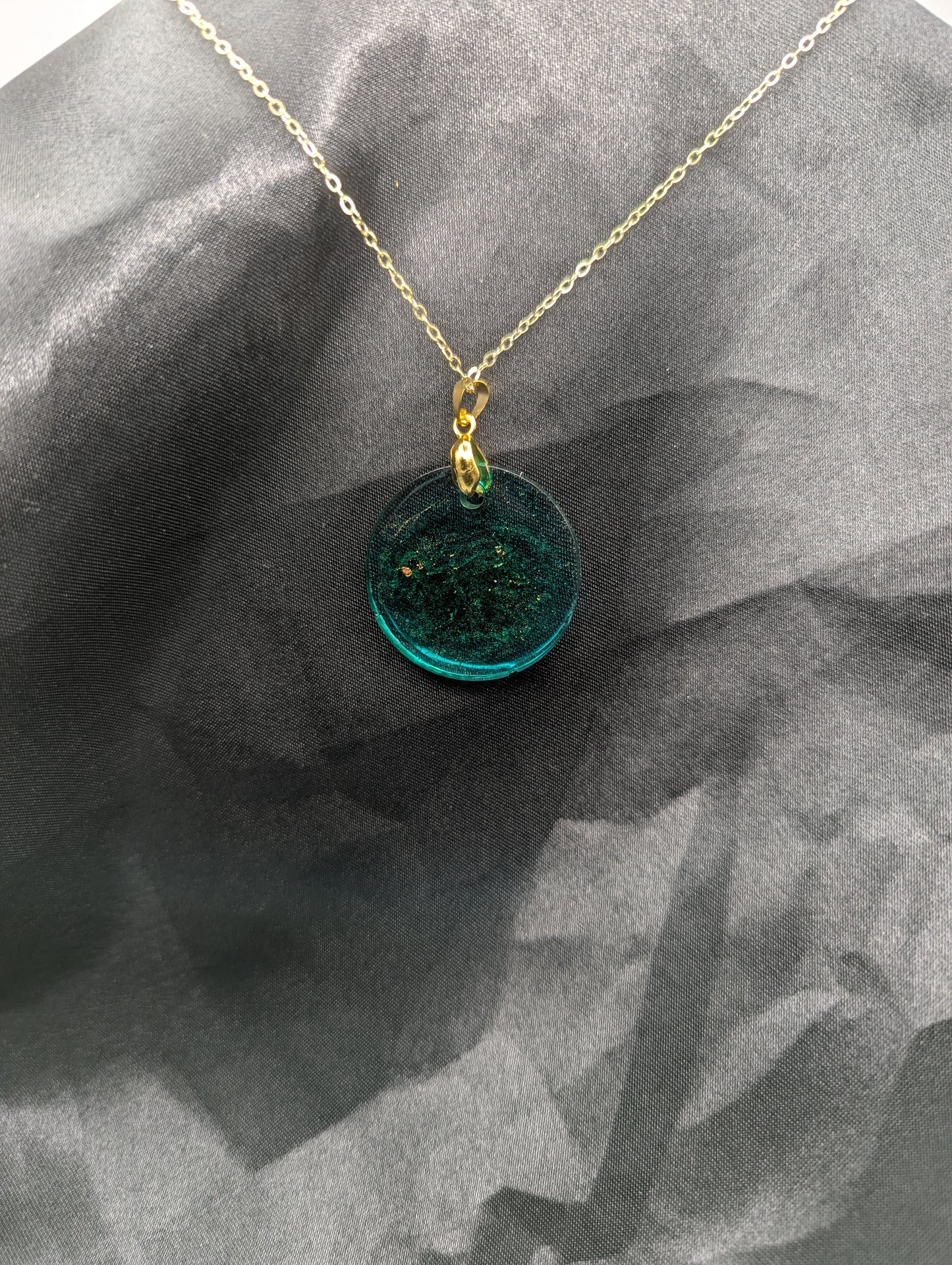 Back view of Emerald green circle resin pendant swirled with gold pigment on a gold pinch bail with a gold plated metal chain.