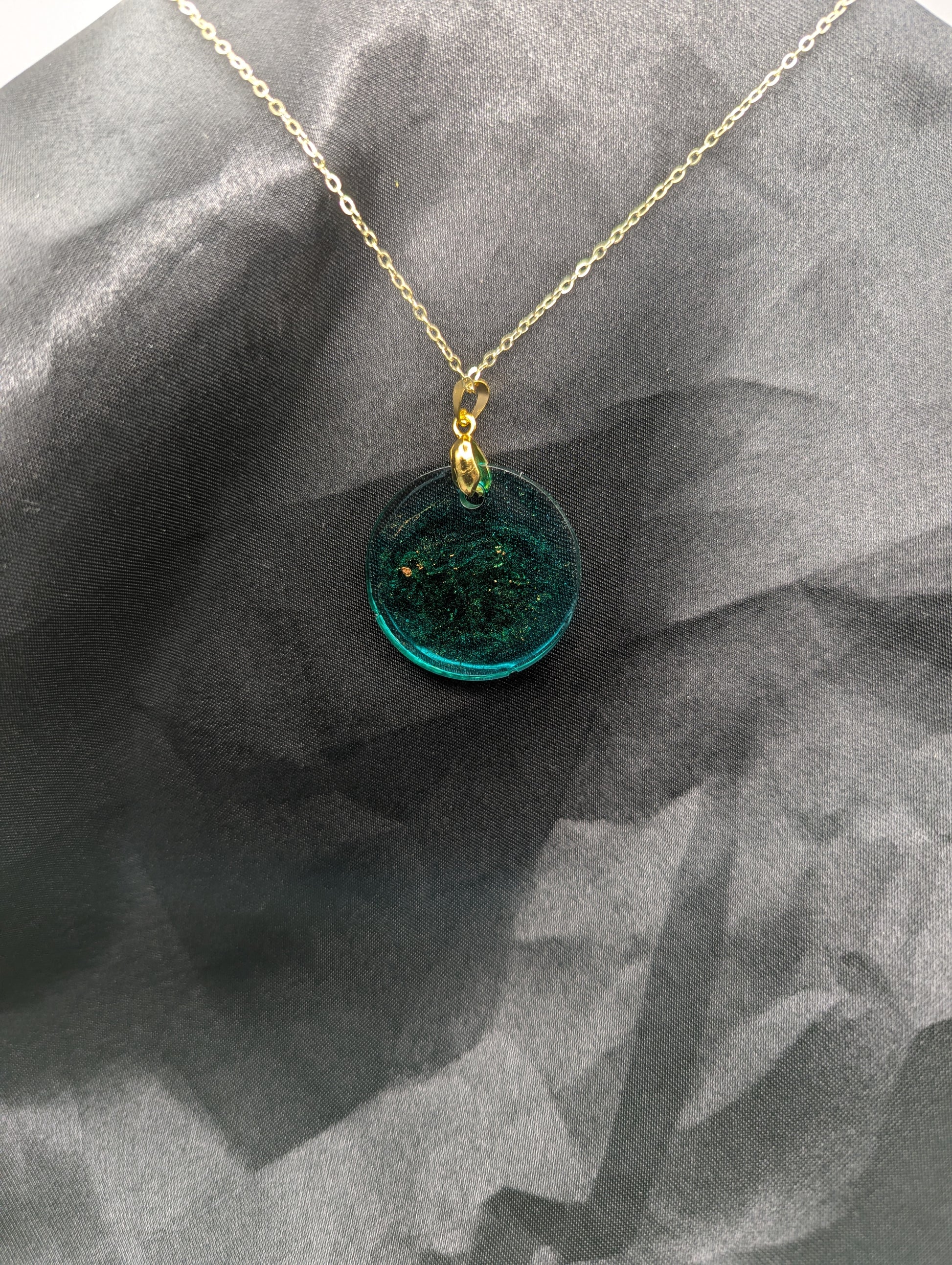 Back view of Emerald green circle resin pendant swirled with gold pigment on a gold pinch bail with a gold plated metal chain.