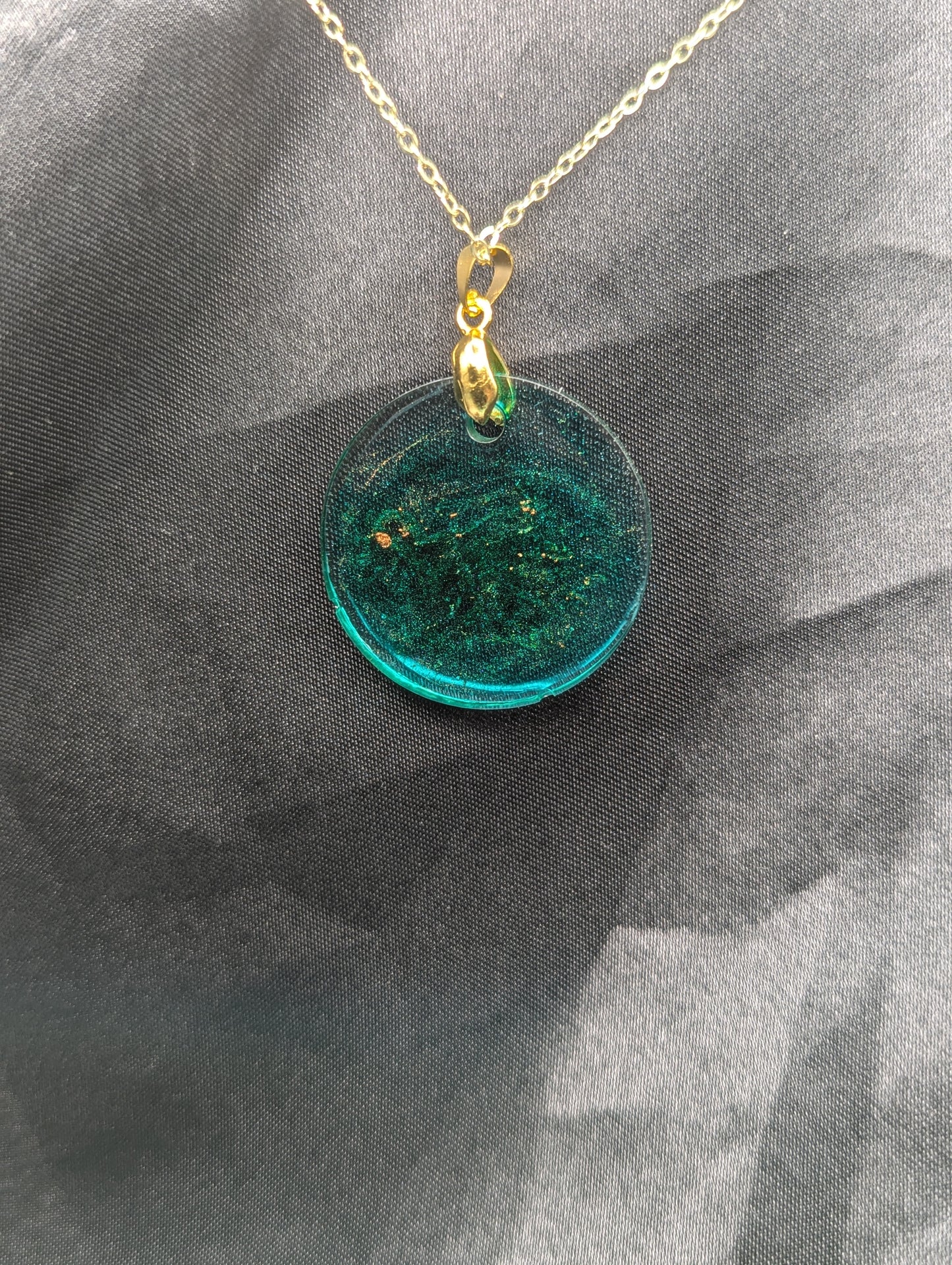Back view of Emerald green circle resin pendant swirled with gold pigment on a gold pinch bail with a gold plated metal chain.