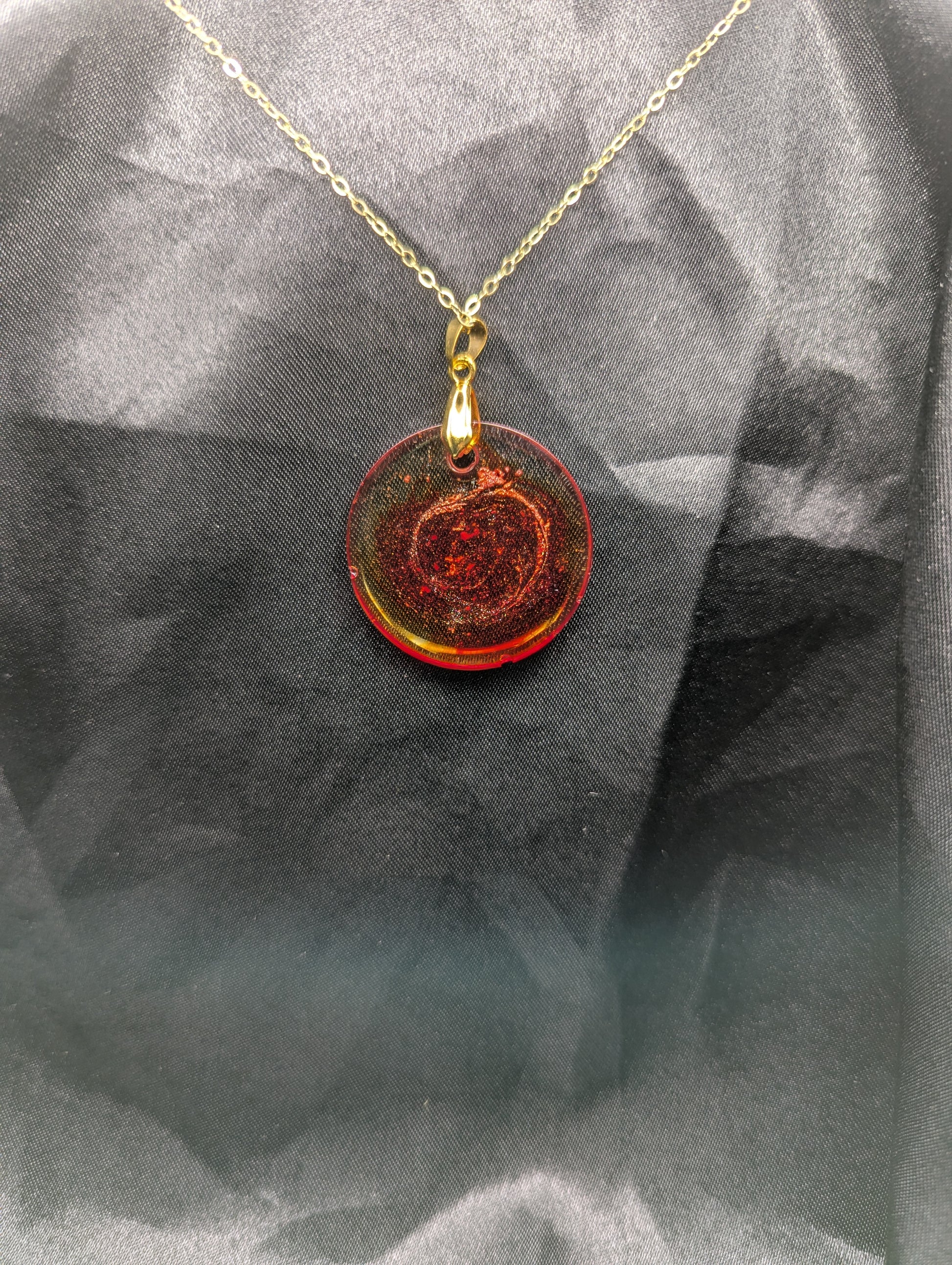 Back view of Red colored circle resin pendant with a coral colored pigment swirled in it, with a gold pinch bail on a gold plated metal chain.