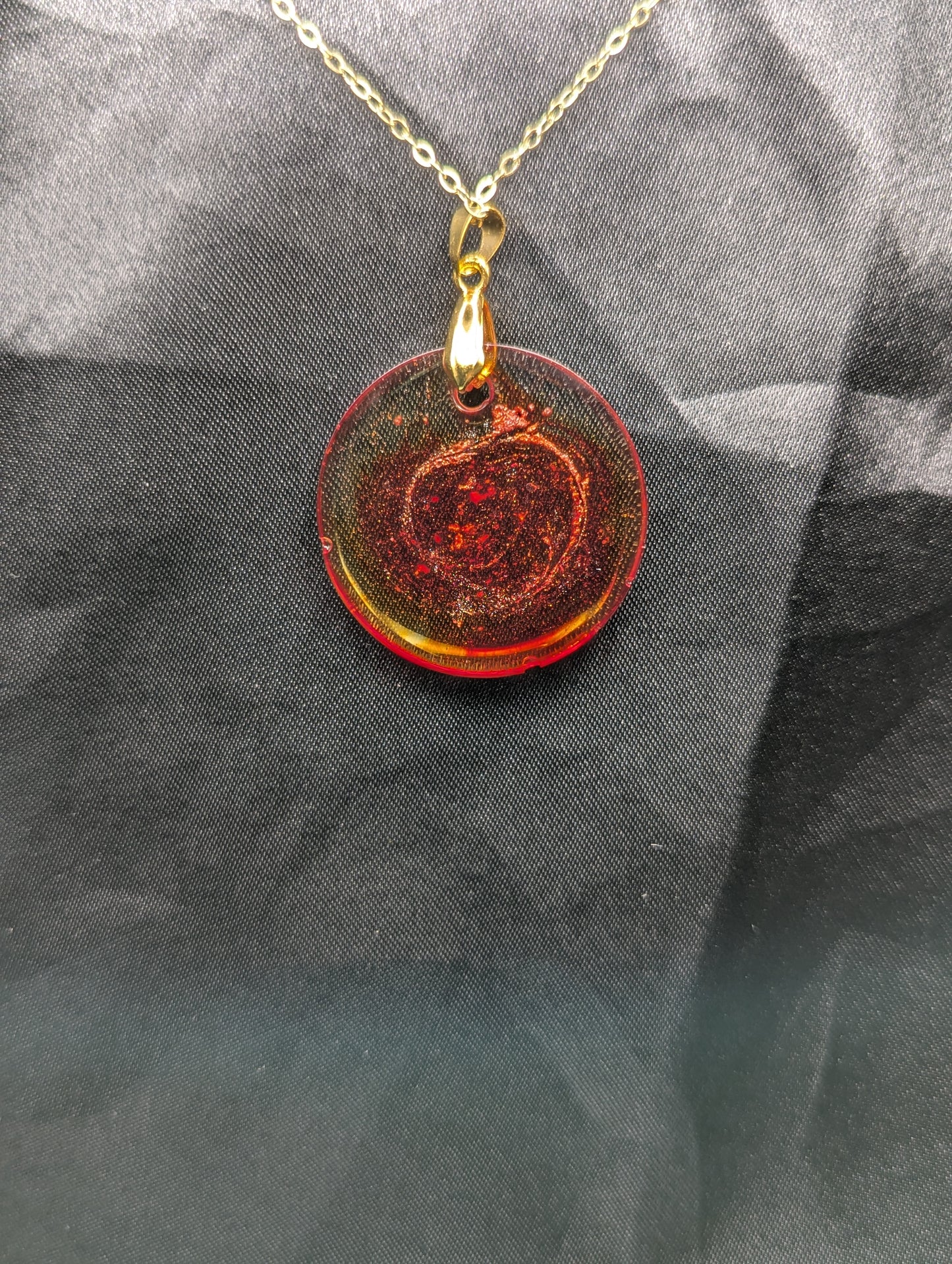 Back view of Red colored circle resin pendant with a coral colored pigment swirled in it, with a gold pinch bail on a gold plated metal chain.